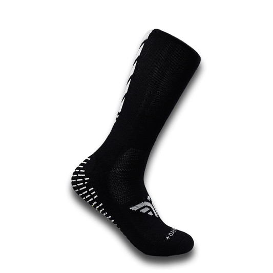 A black For The Footballer XLR8R Pro No Slip Sock featuring white logo details and rubberized grip pads on the heel and sole.