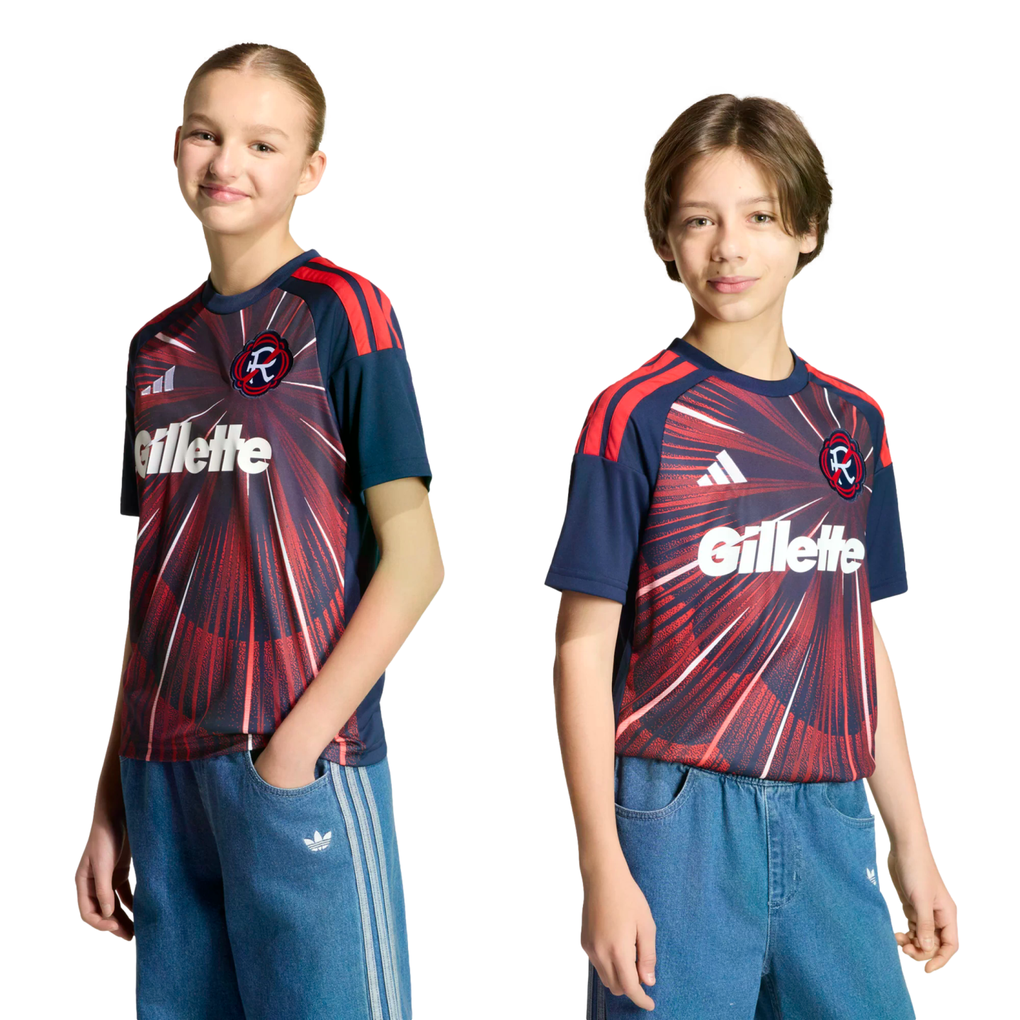 Two children pose in matching navy and red soccer jerseys and blue denim Adidas pants against a black background.