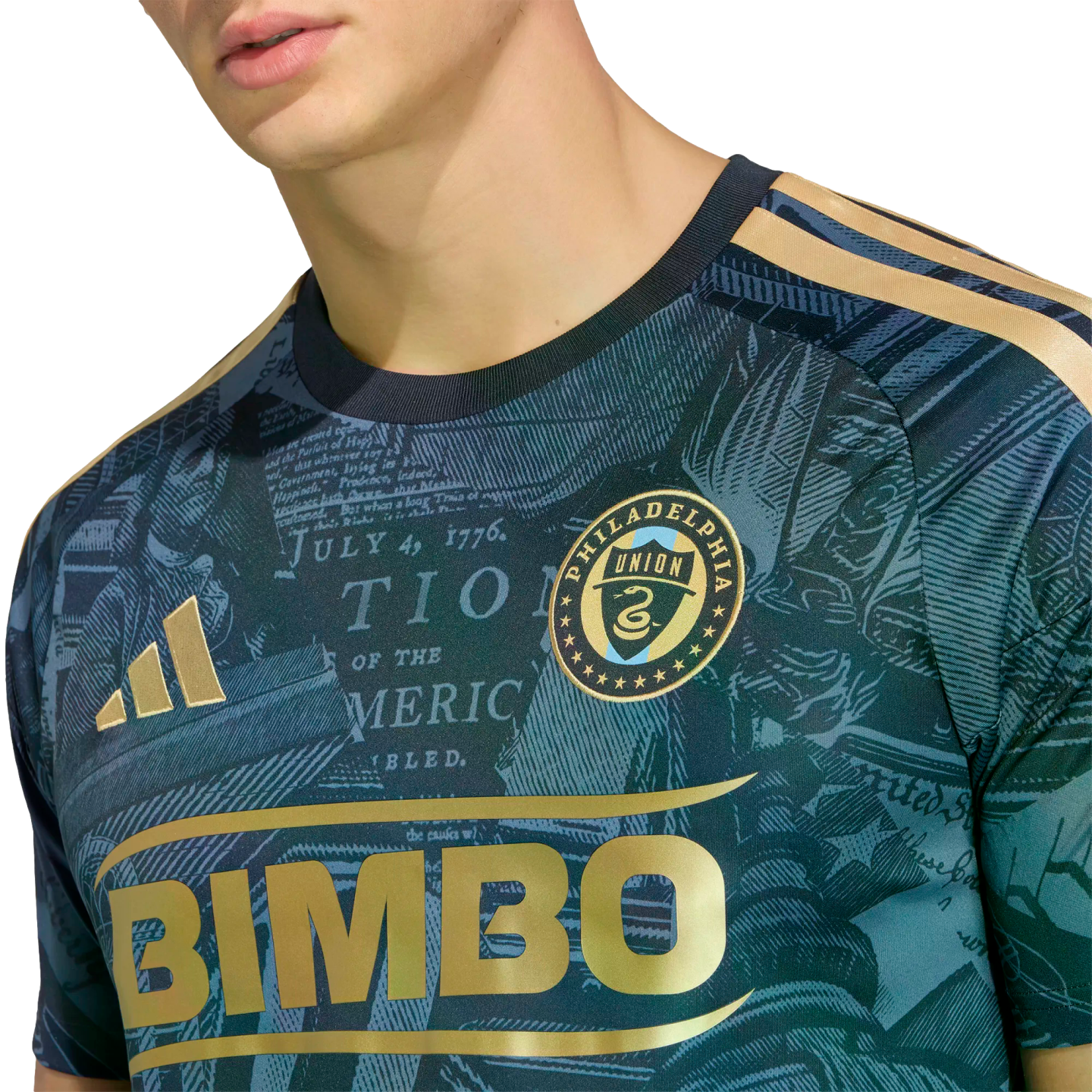 Close-up of a Philadelphia Union soccer jersey with a gold "BIMBO" logo, team crest, and a teal background patterned with historical text.