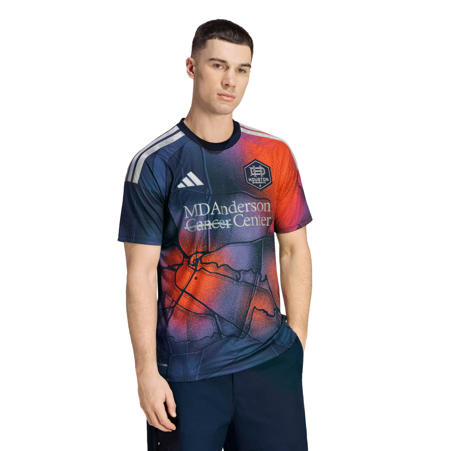 A man models a navy Houston Dynamo FC soccer jersey featuring a red and orange map pattern and the MD Anderson Cancer Center logo.