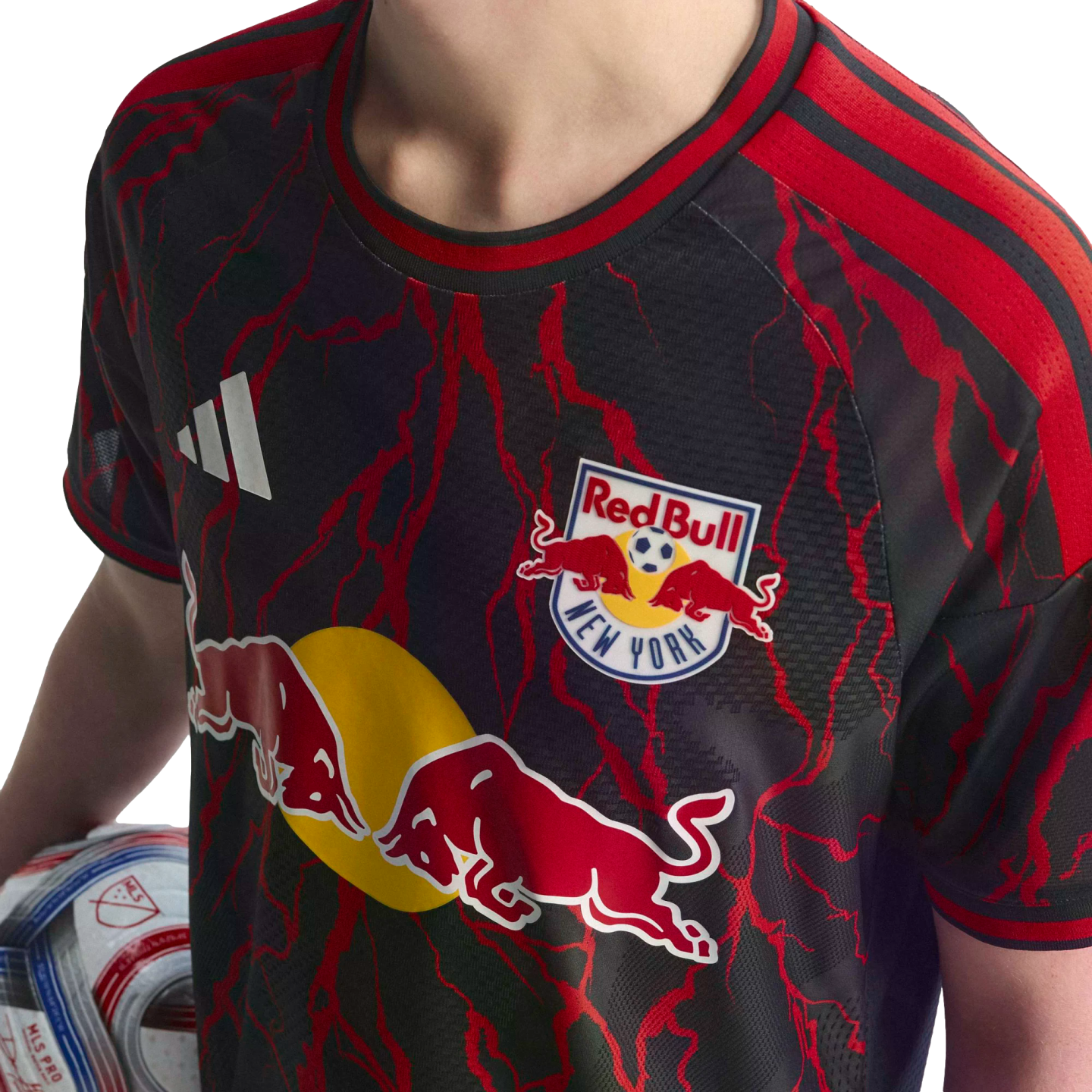 A person wears a black New York Red Bulls soccer jersey with red lightning patterns and prominent team logos, while holding an MLS soccer ball.