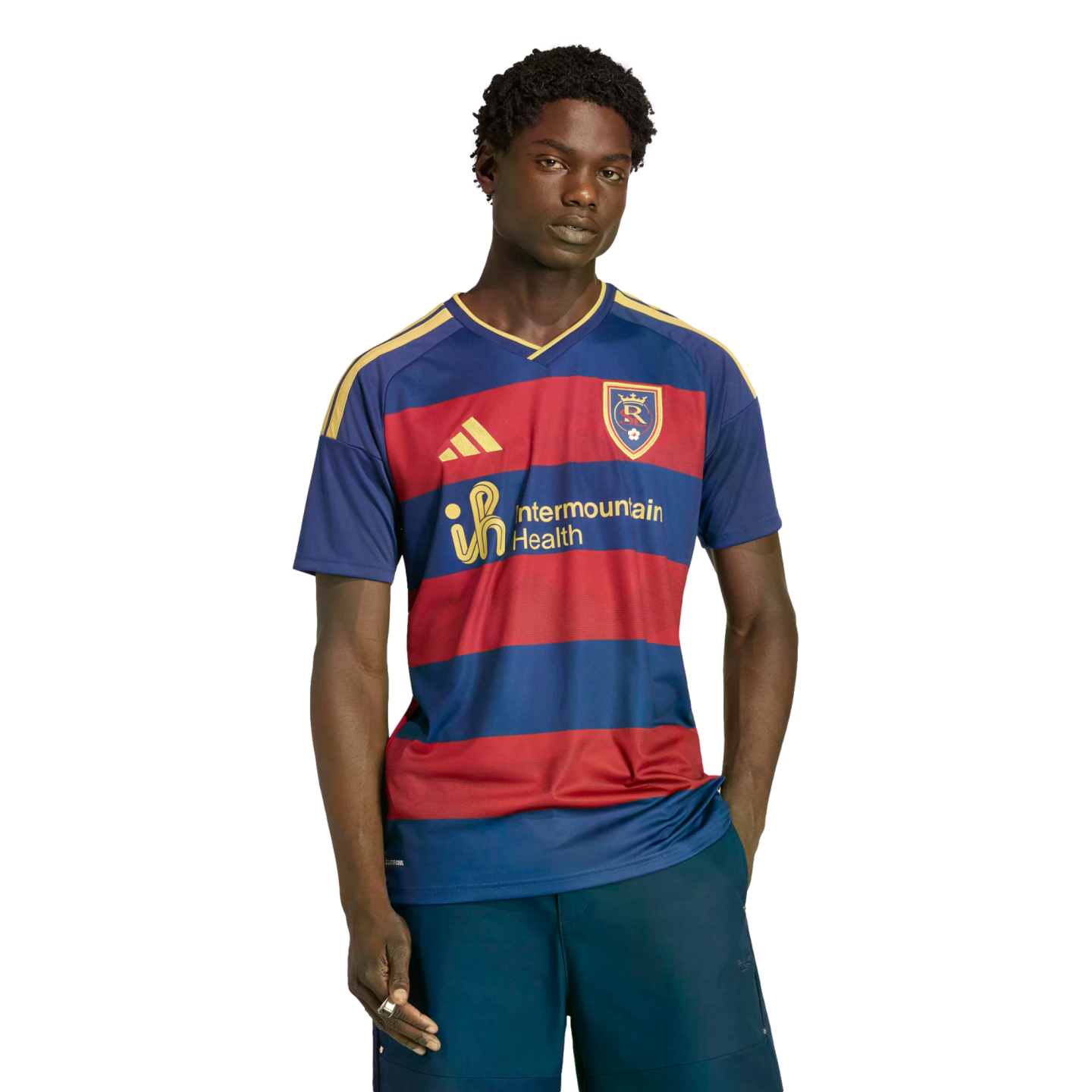 A young man models a Real Salt Lake soccer jersey with red and blue stripes and yellow accents against a black background.