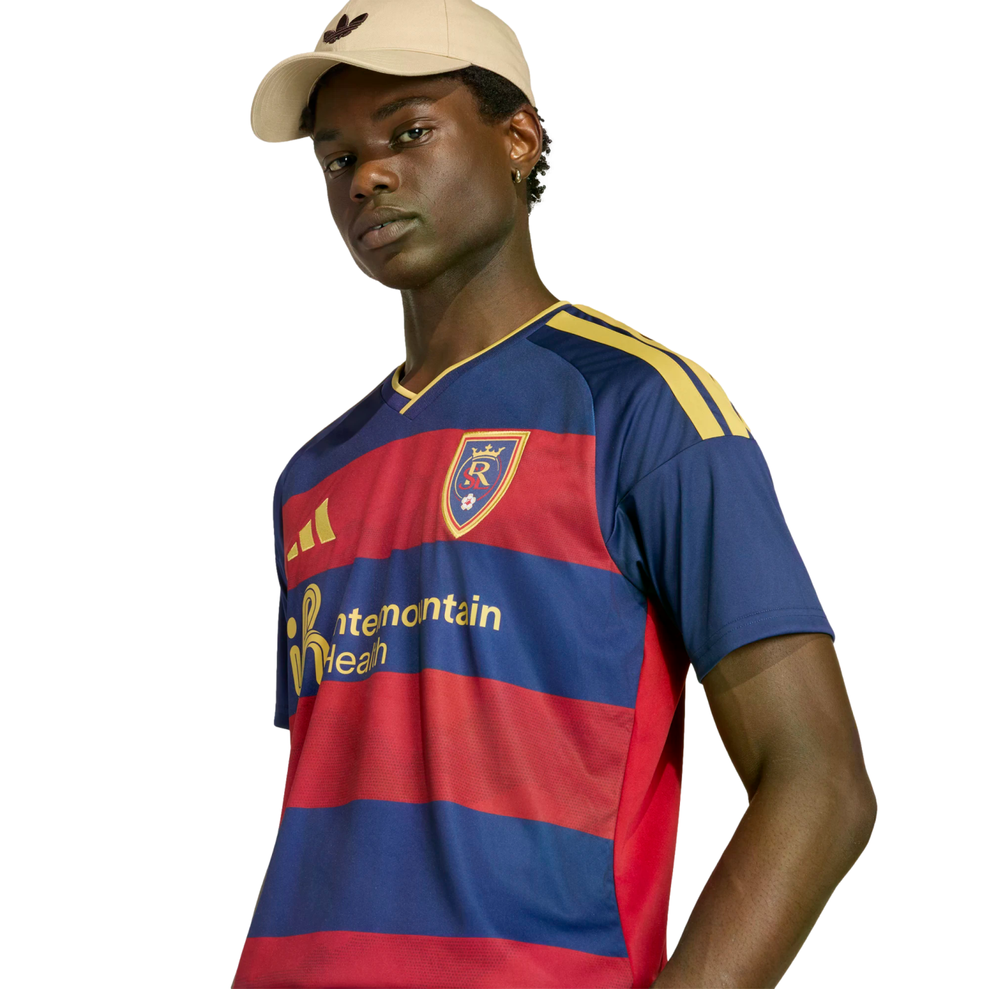 A man in a beige cap and a navy and red striped Real Salt Lake soccer jersey with yellow accents, posed against a black background.