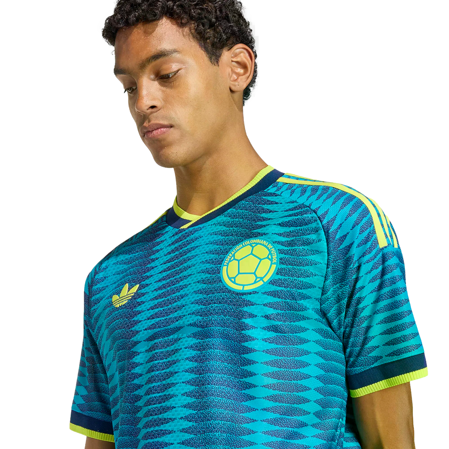 Young man wearing a blue and yellow Colombia soccer jersey with a wavy pattern, looking down against a black background.