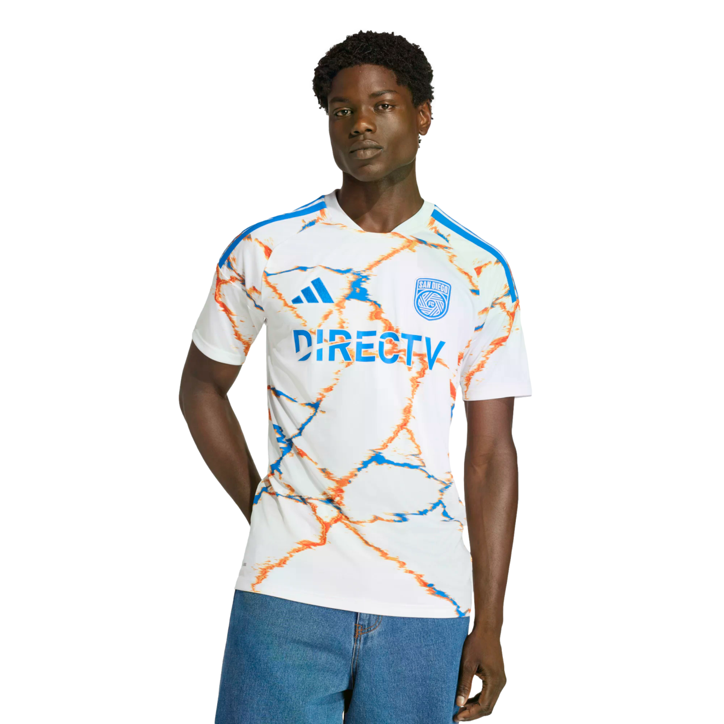 A man in a white San Diego FC soccer jersey with orange and blue patterns and "DIRECTV" sponsor, wearing blue jeans against a solid black background.