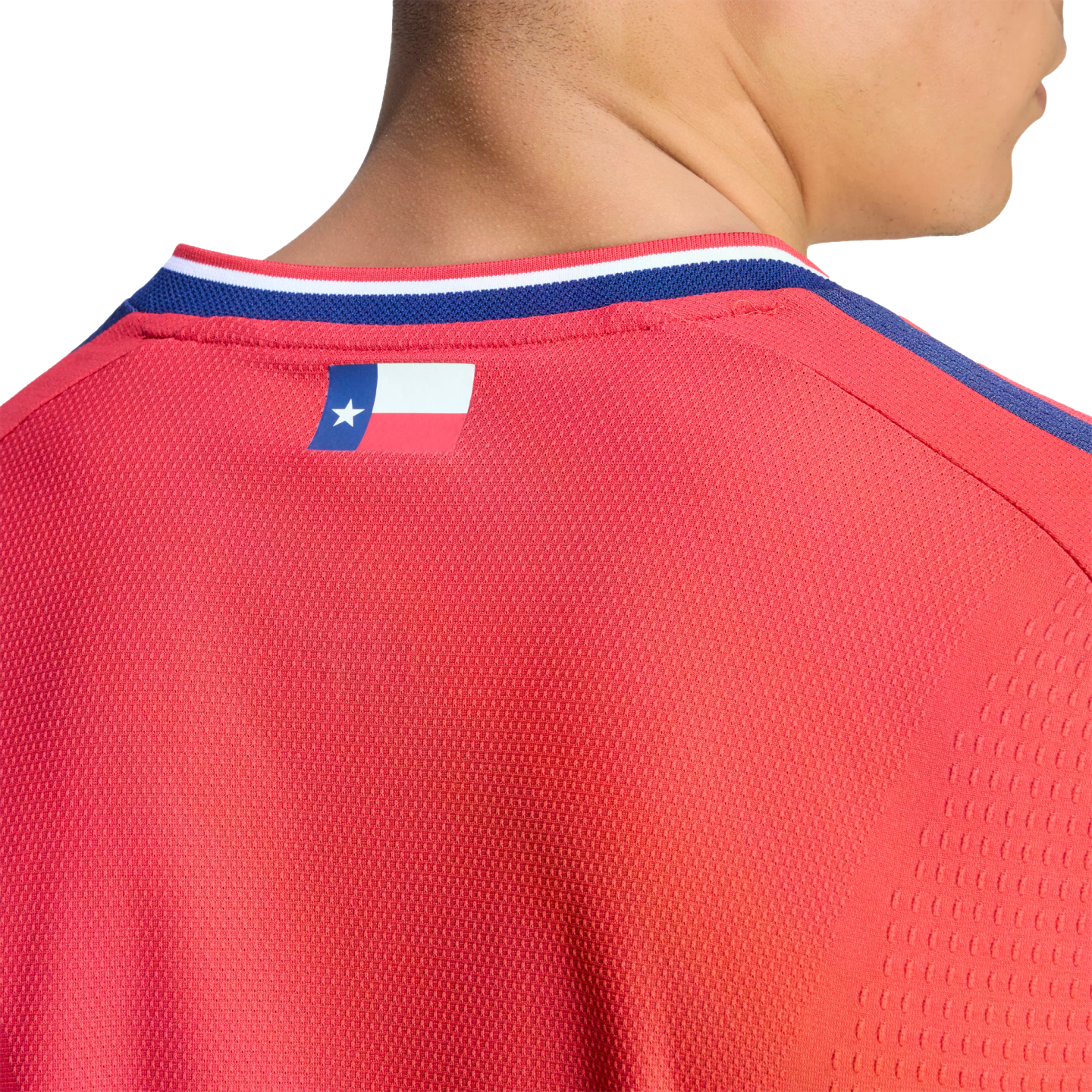 Close-up of a person wearing a red textured sports jersey with a small Texas flag logo on the upper back, just below the striped collar.