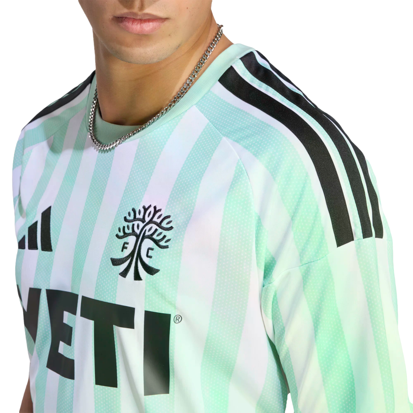 Close-up of a man wearing a light green and white striped Austin FC soccer jersey with a silver chain, set against a black background.