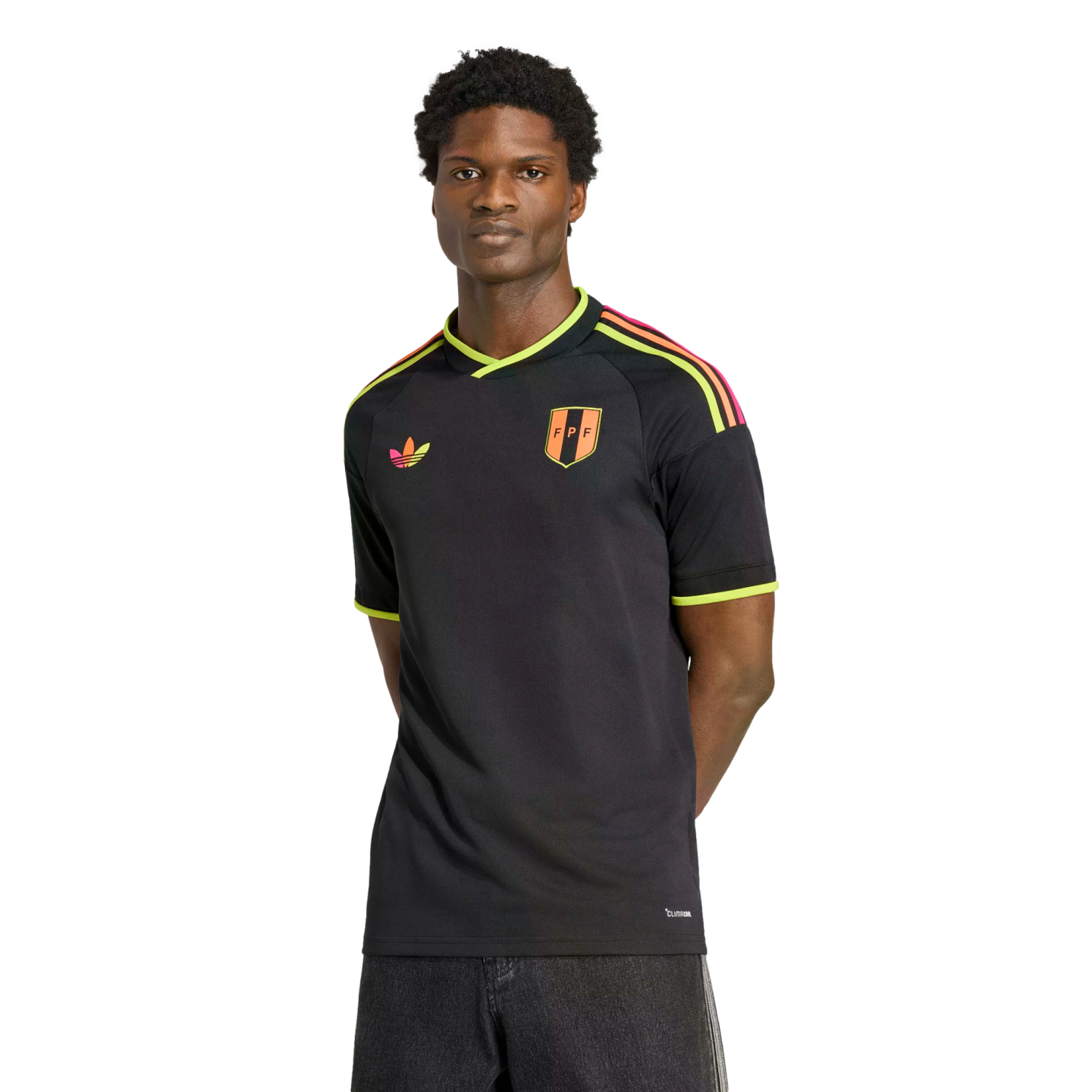 A man wears a black Adidas soccer jersey with neon lime and pink accents and an "FPF" crest. He is posed with hands behind his back against a solid black background.