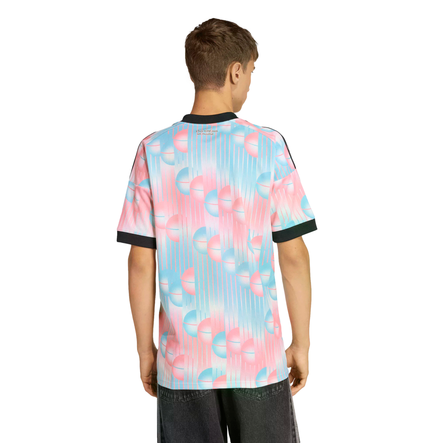 A man from behind in a t-shirt with a pink and blue spherical pattern and black trim, paired with dark jeans, set against a black background.