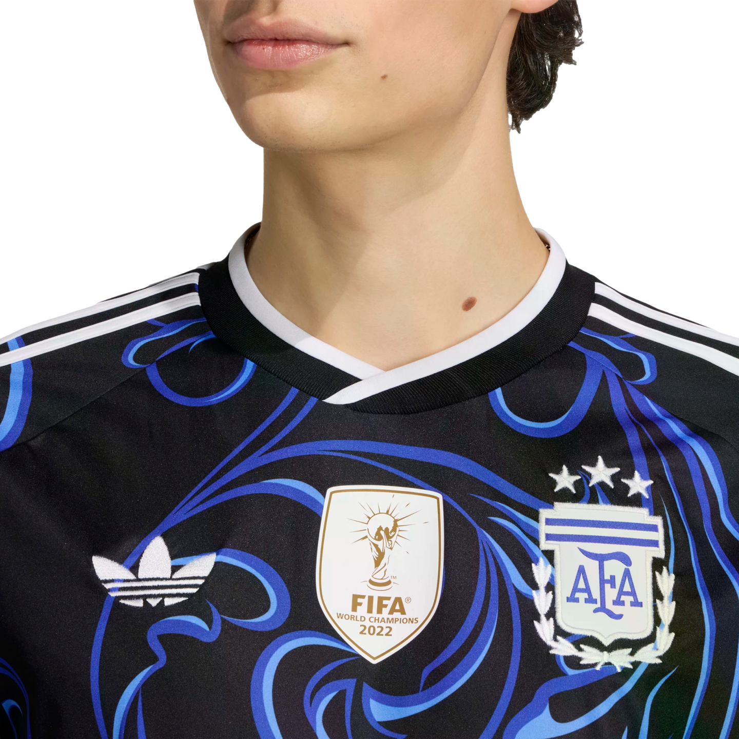 Close-up of a person in a black and blue patterned Argentina jersey featuring the 2022 FIFA World Champions patch, Adidas Trefoil logo, and the AFA crest with three stars.