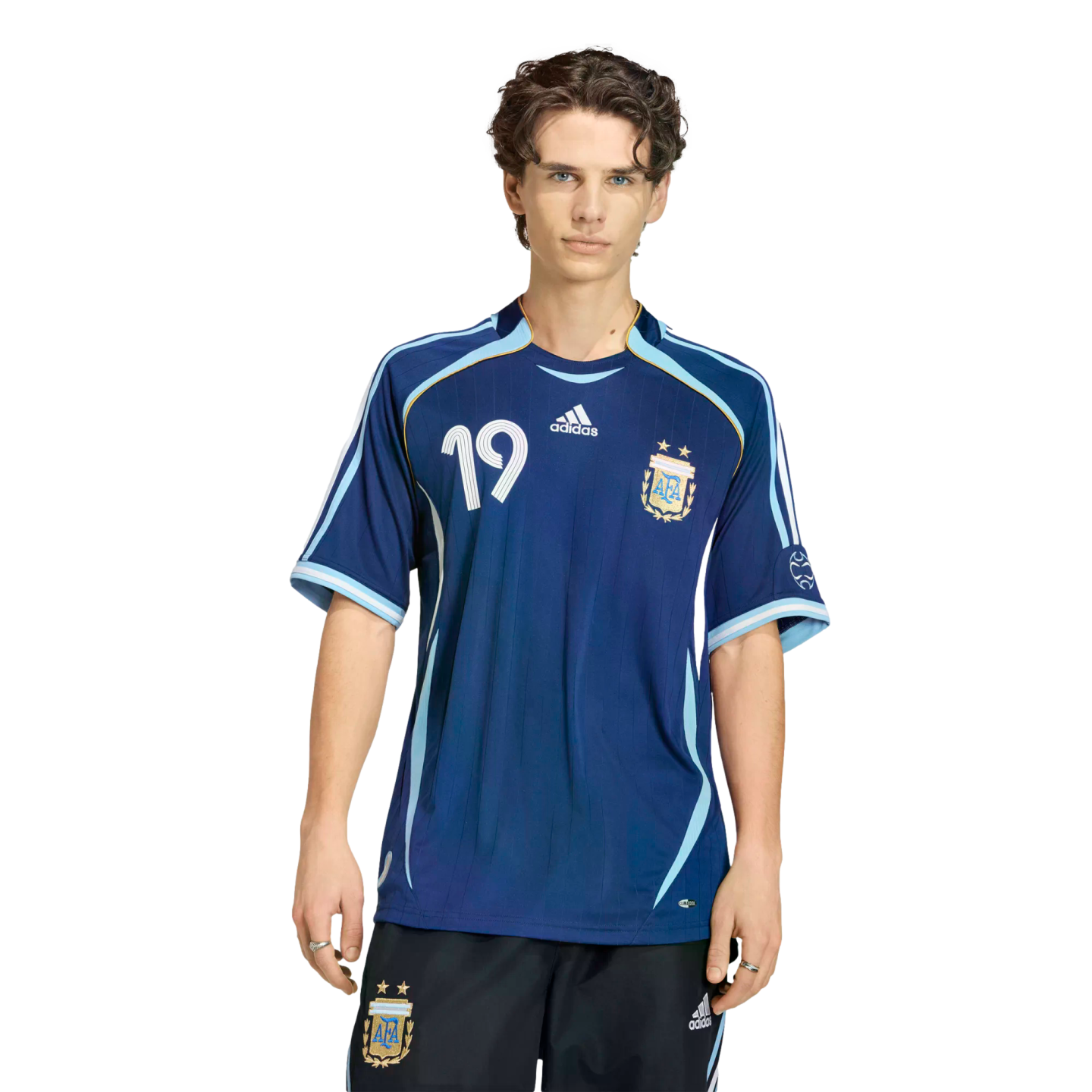 Young man posing in a dark blue Argentina soccer jersey with number 19 and matching shorts against a solid black background.