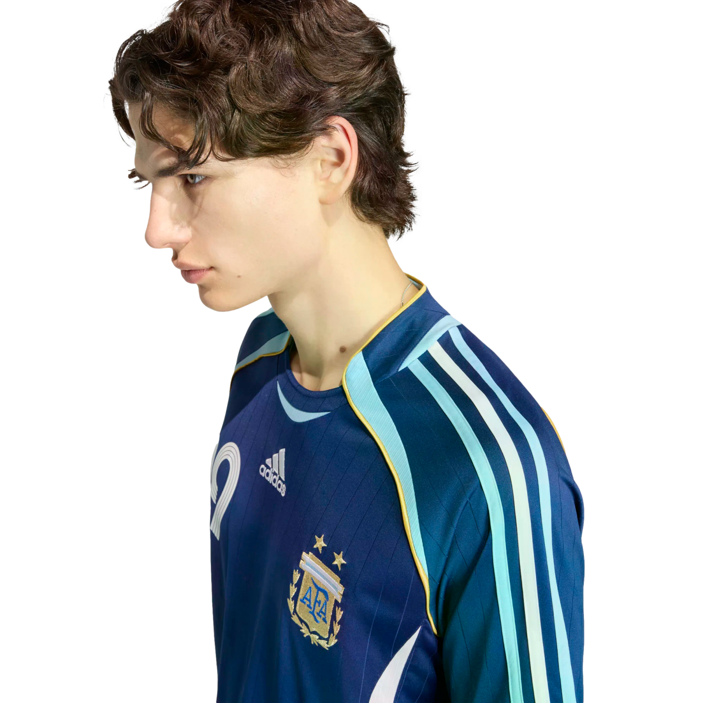 Profile of a young man with wavy brown hair wearing a navy blue Argentina national team soccer jersey against a solid black background.