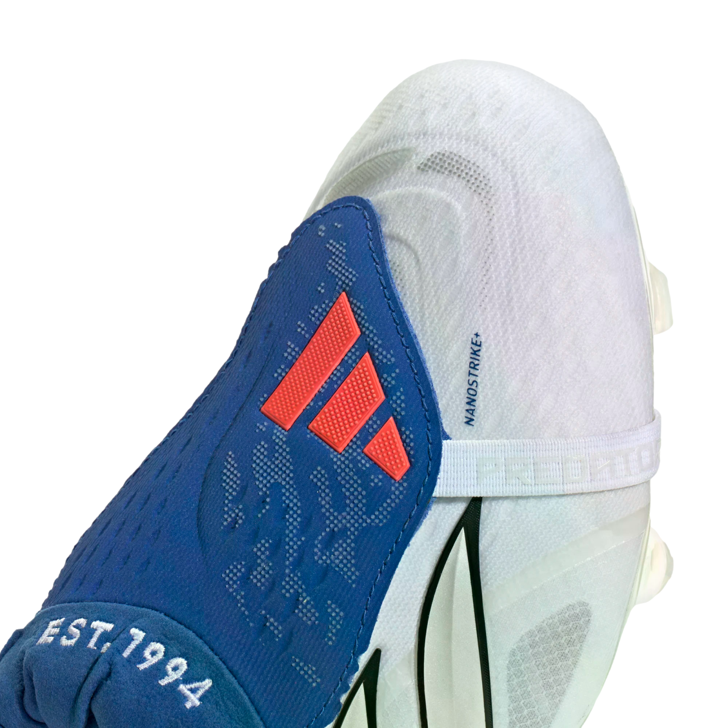 White and blue Adidas soccer cleat featuring a blue tongue with a red logo and white "EST. 1994" embroidery against a black background.