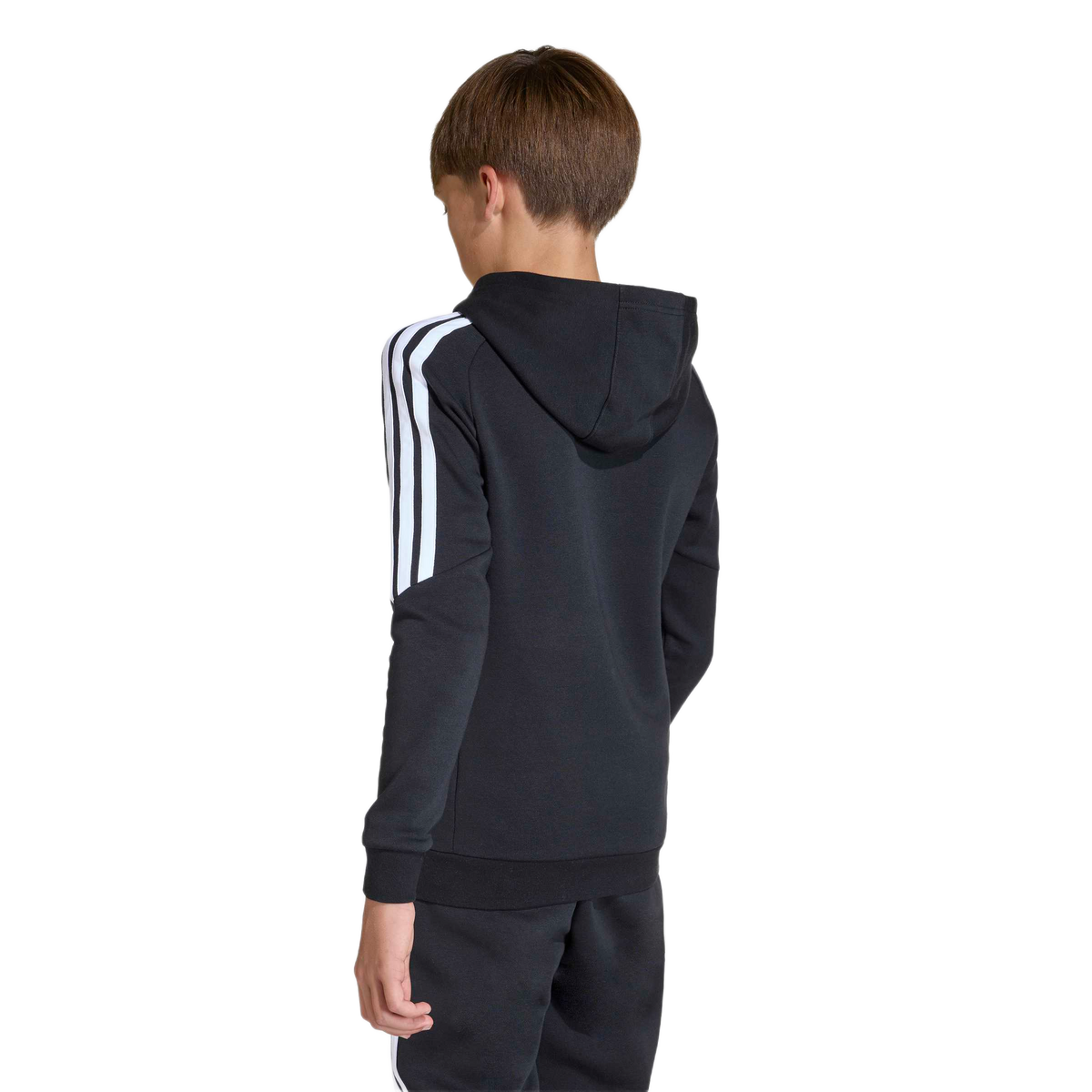Rear view of a boy in a black Adidas hoodie with white stripes on the sleeves and matching sweatpants, standing against a plain light gray background.