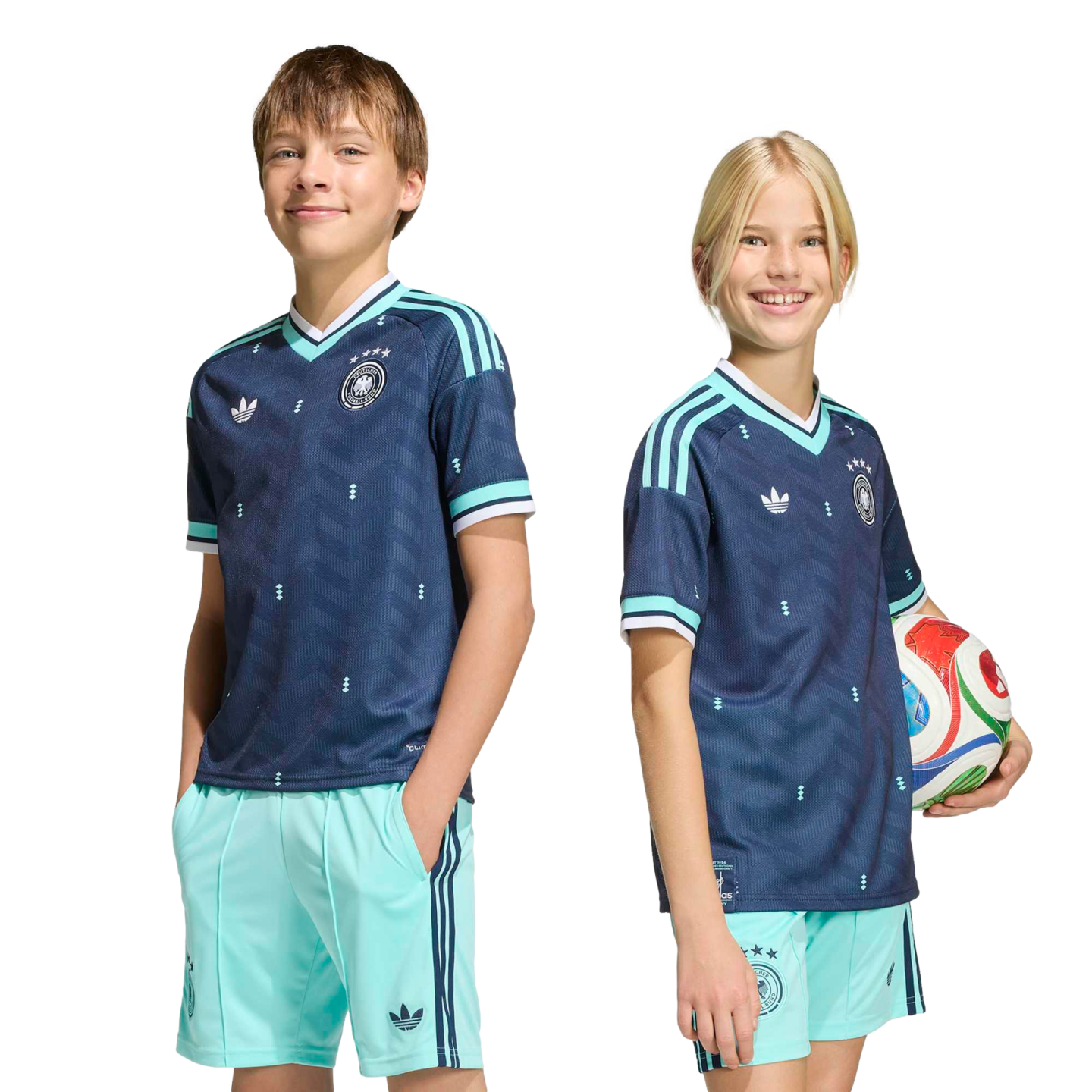 A boy and a girl smile while wearing matching navy blue and light blue Adidas soccer kits. The girl holds a soccer ball against a solid black background.
