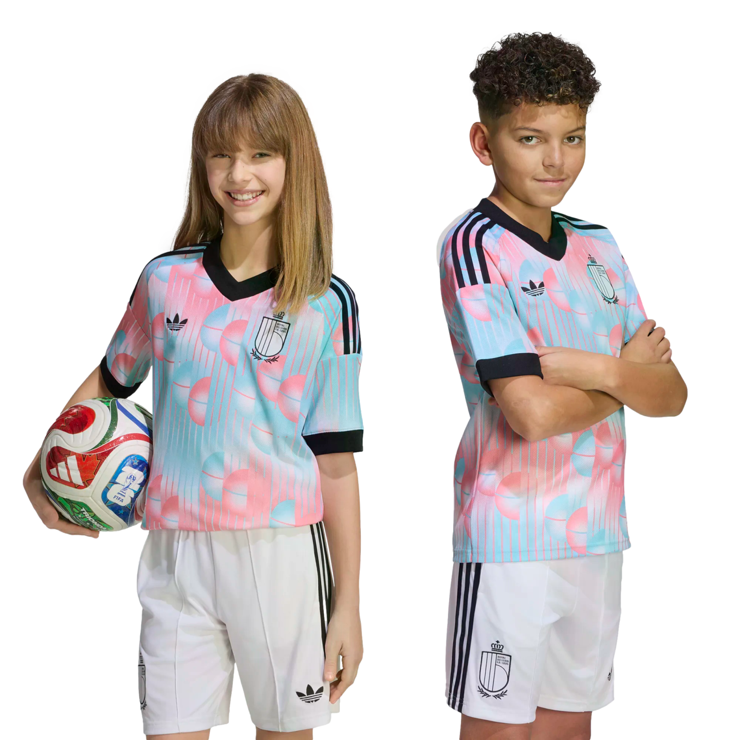 A boy and girl in matching pink and blue patterned soccer jerseys and white shorts pose against a black background. The girl holds a soccer ball.