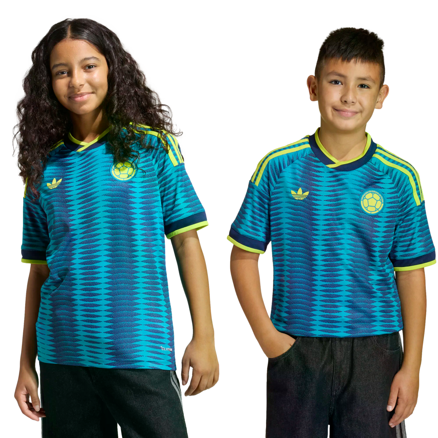 Two children smile while wearing matching teal and blue patterned Colombia national team soccer jerseys with yellow accents.