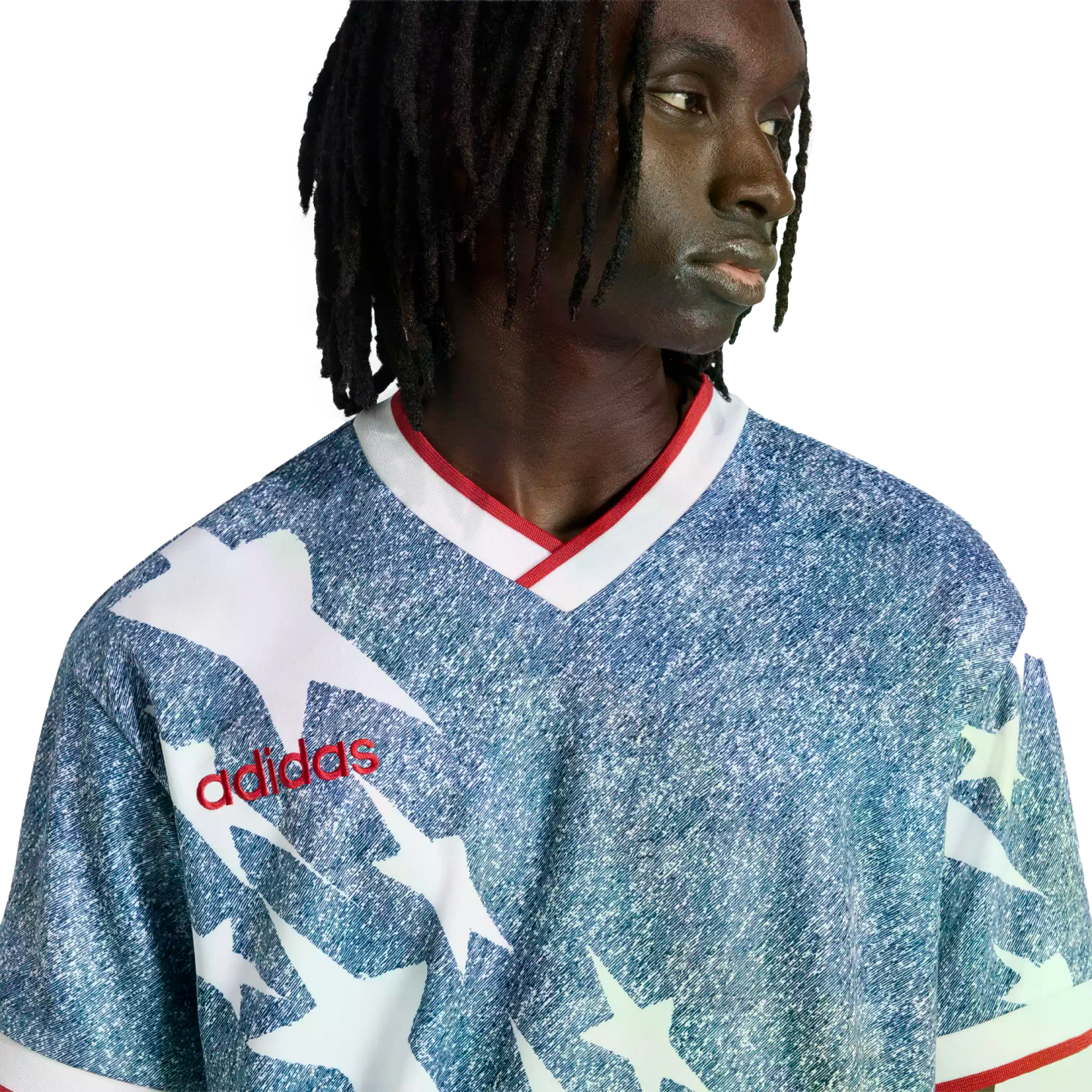 A person with dreadlocks wears a blue and white star-patterned Adidas jersey with a red logo and collar, set against a solid black background.