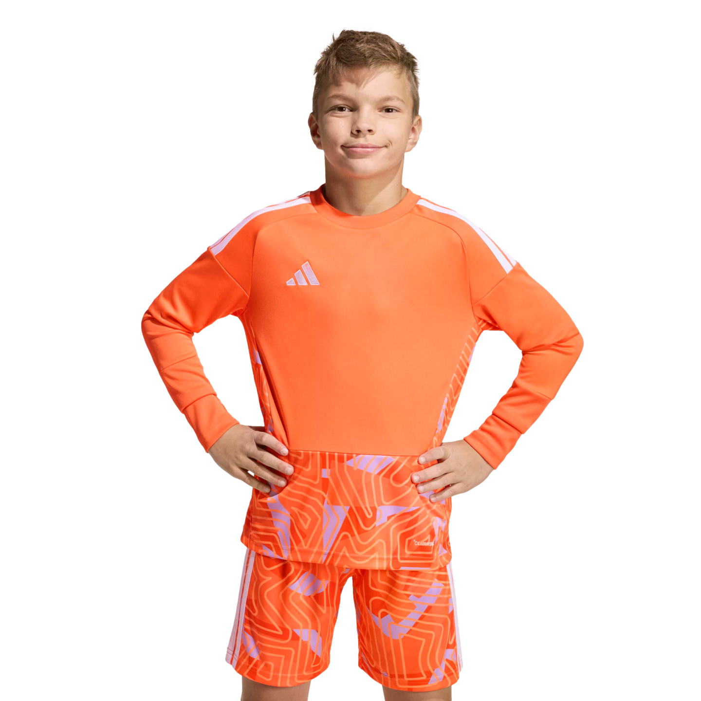 Boy in an orange long-sleeved Adidas soccer kit with a geometric pattern, posing with hands on hips against a solid black background.