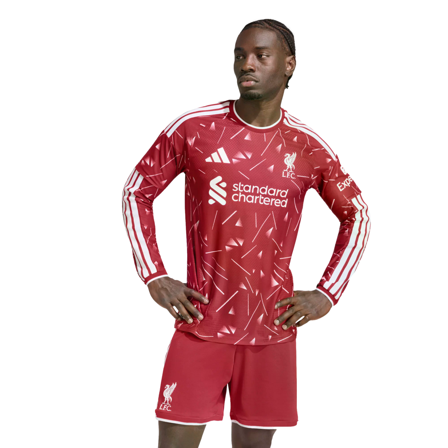 A man wearing a red and white patterned long-sleeved Liverpool F.C. jersey and matching shorts stands with his hands on his hips against a white background.