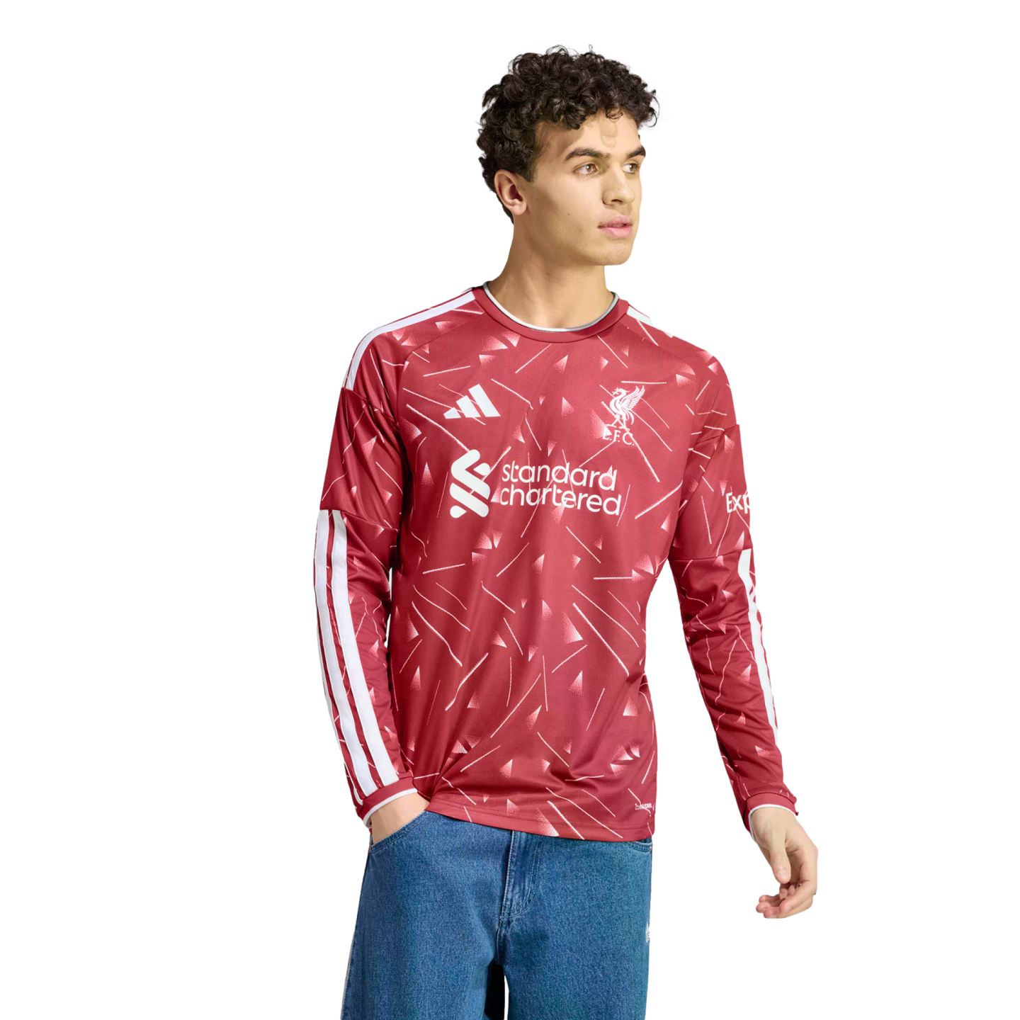 A young man wearing a red long-sleeved Liverpool FC jersey with white patterns and logos, paired with blue jeans, set against a white background.