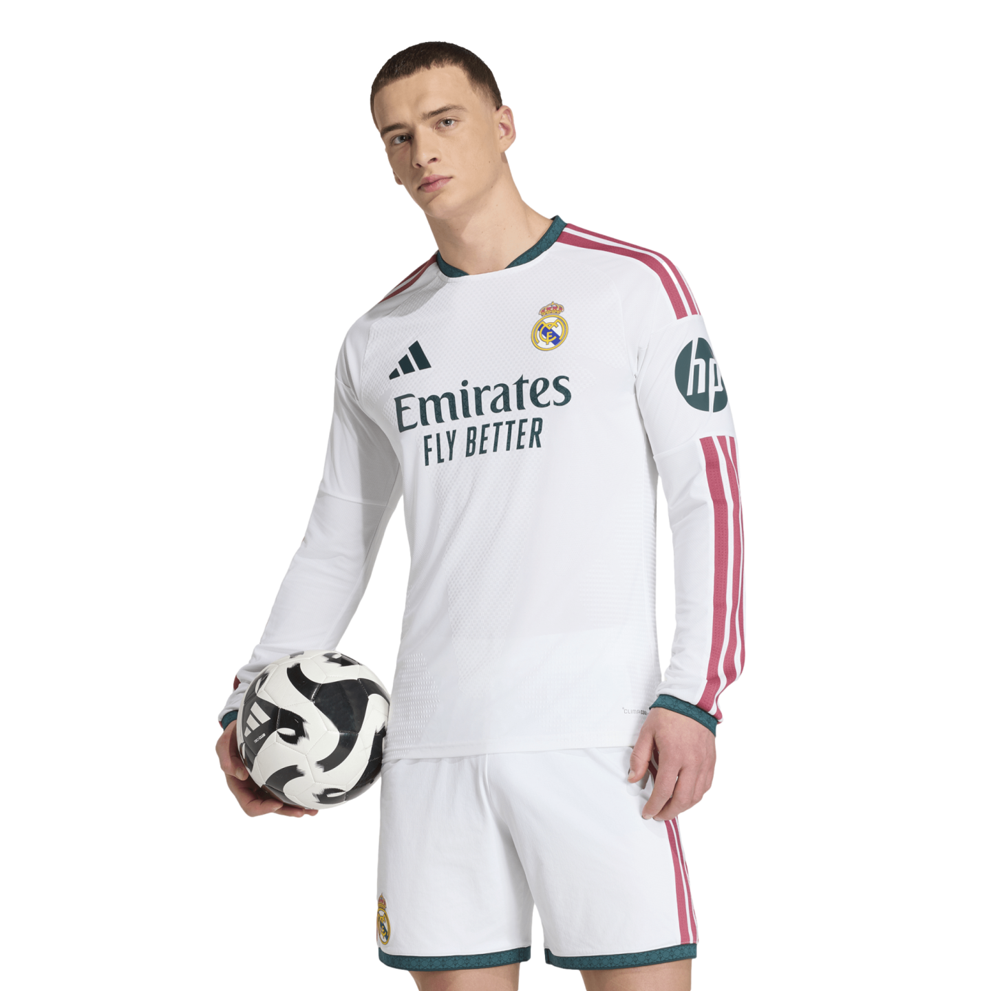 A man in a white Real Madrid long-sleeve jersey and shorts holds a soccer ball against a plain white background.