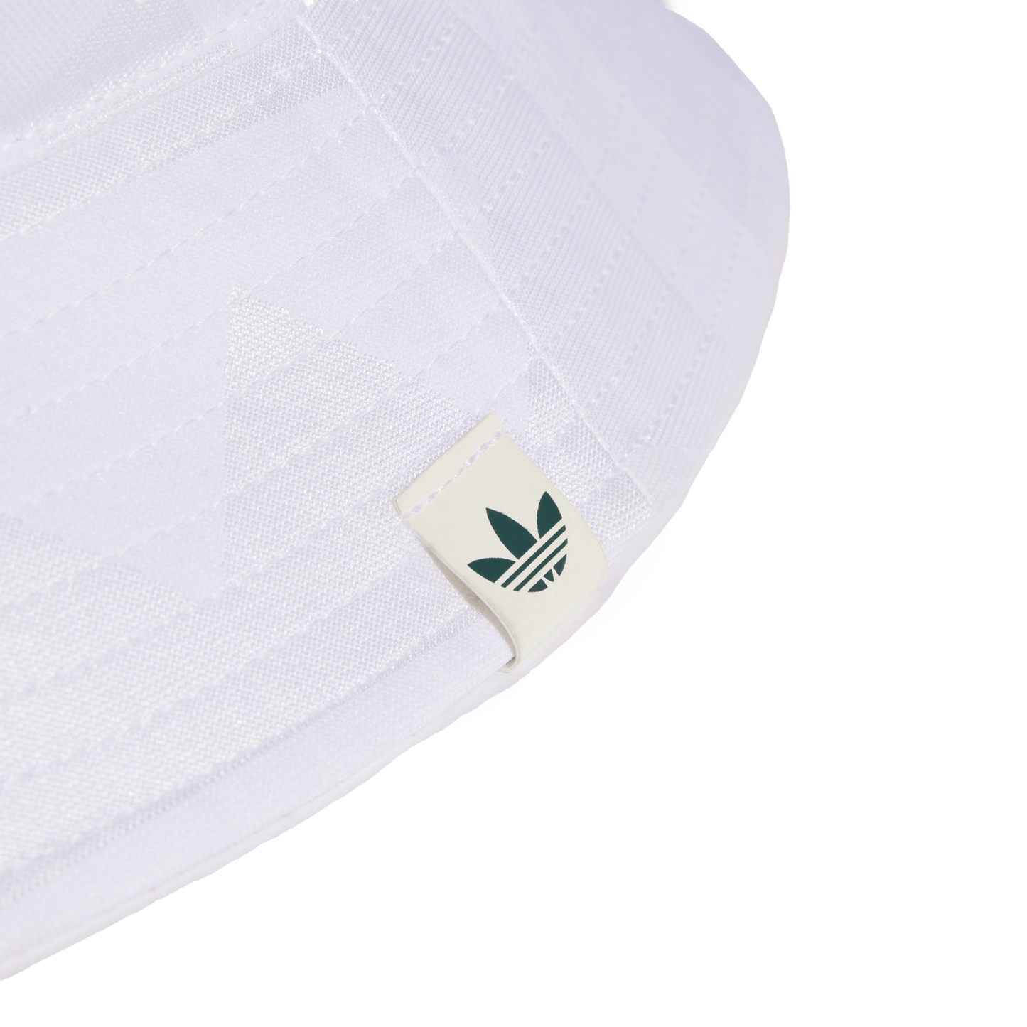 Close-up of the brim of a white bucket hat featuring a small off-white tag with a dark green Adidas Trefoil logo. Set against a solid black background.