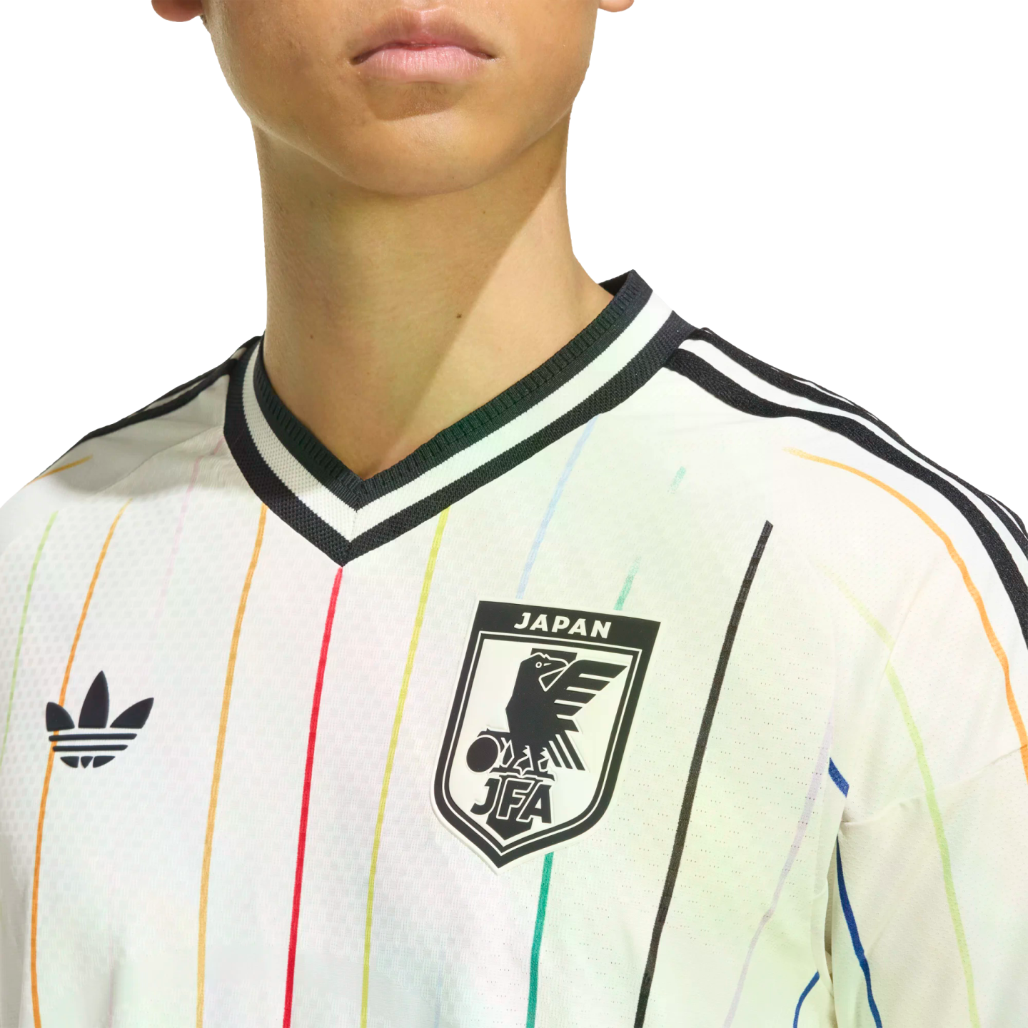 Close-up of a white Adidas Japan jersey with thin vertical rainbow stripes, featuring the Trefoil logo and JFA crest.