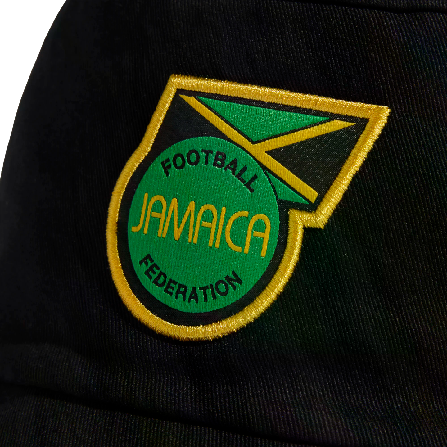 An embroidered Jamaica Football Federation crest on black fabric. The patch features a green circle with the team name and Jamaican flag elements, framed by yellow stitching.