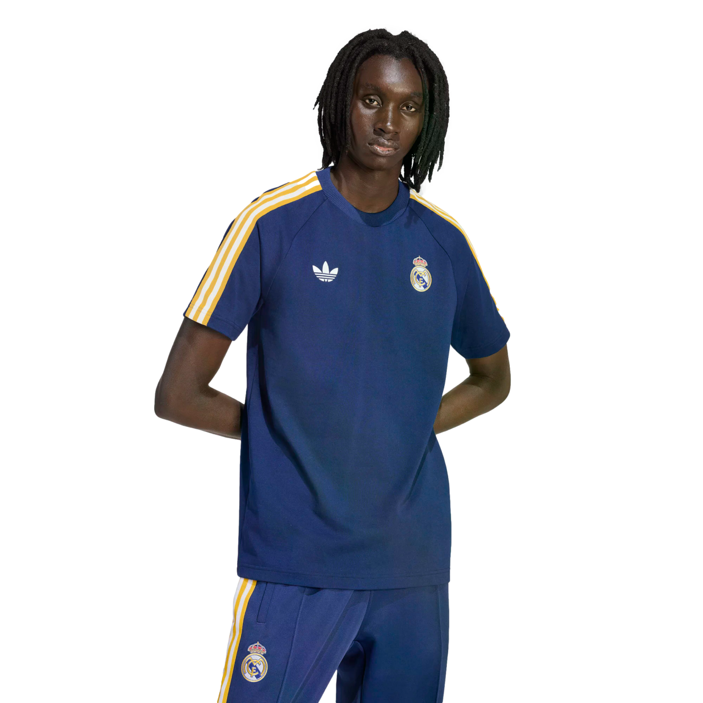 A man wearing a navy blue Adidas Real Madrid t-shirt and matching track pants with yellow and white stripes against a solid black background.