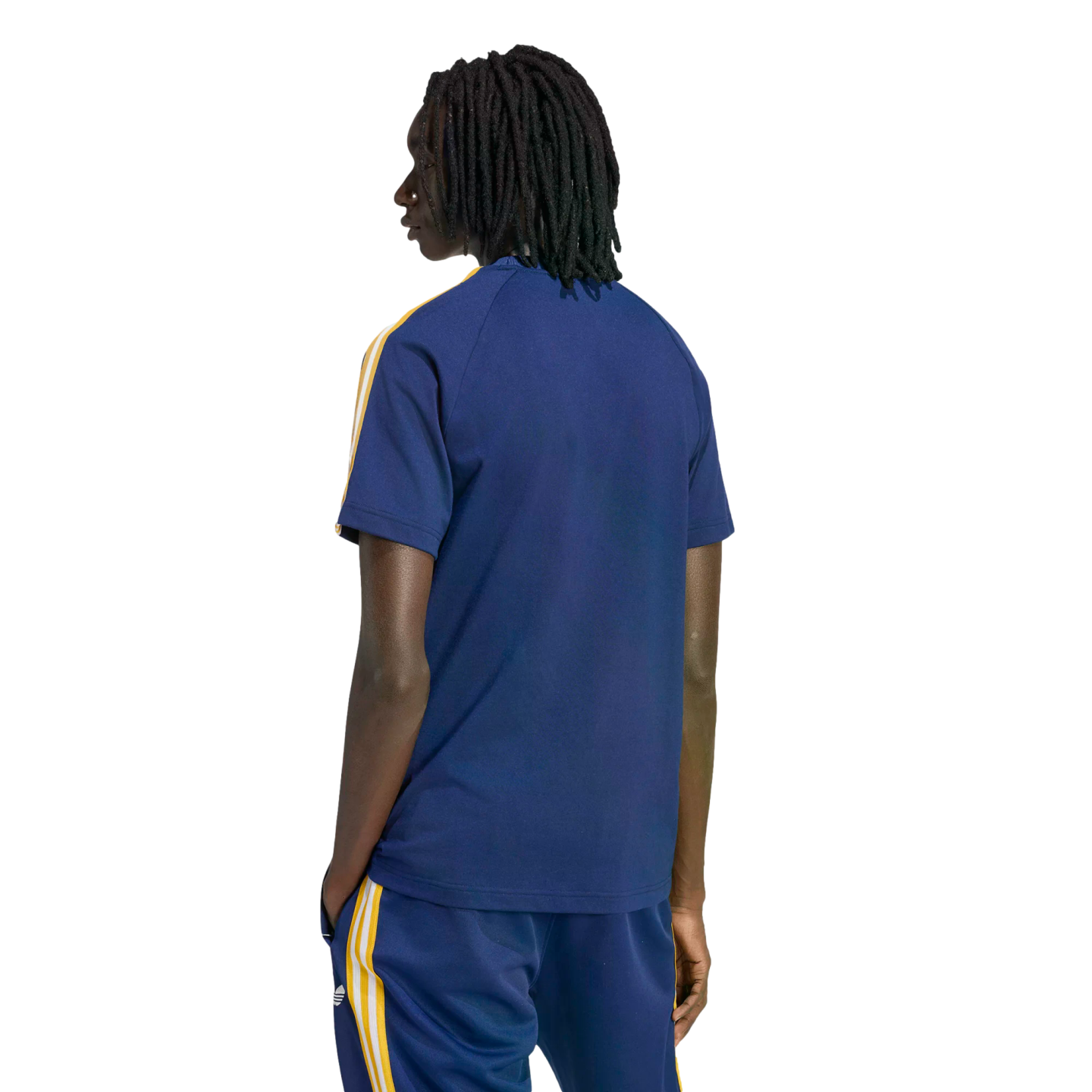 Back view of a person with dreadlocks in a navy blue t-shirt and matching pants with yellow and white stripes, standing against a black background.