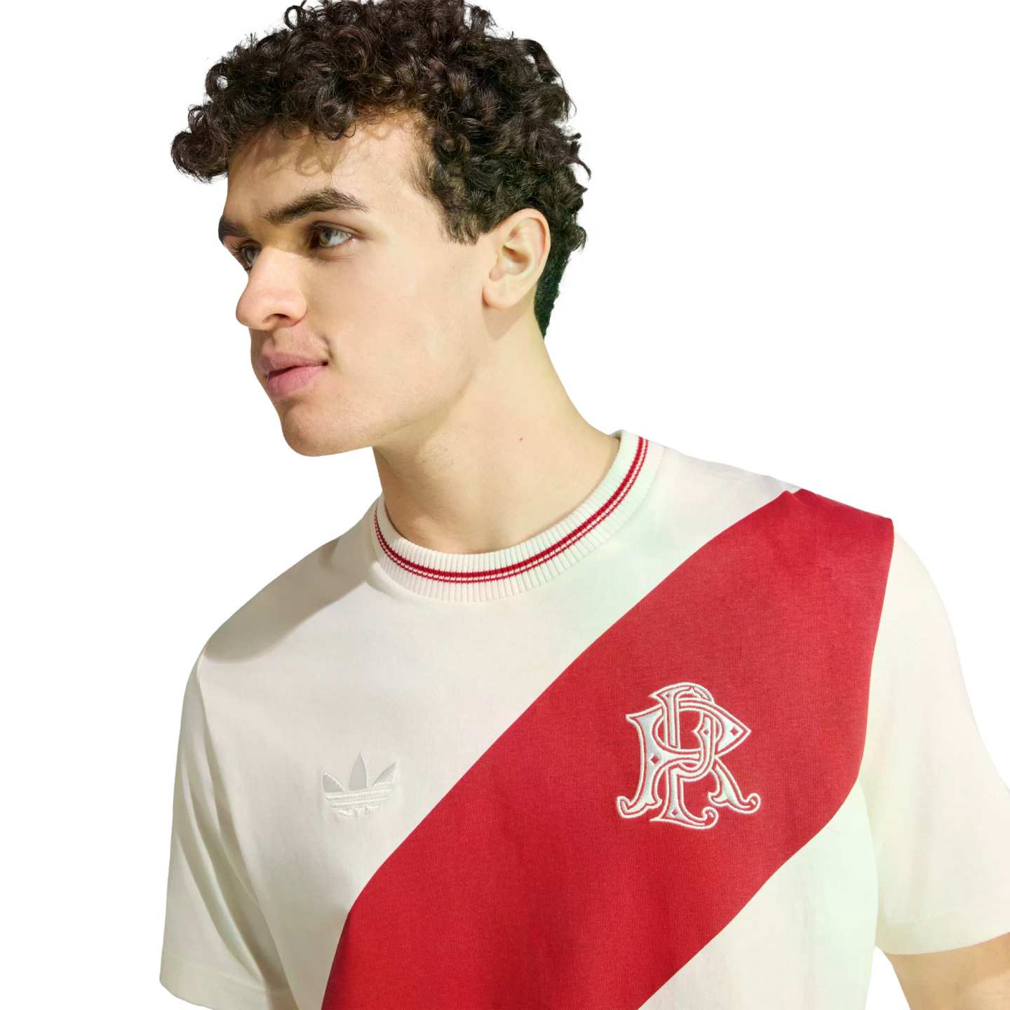 A young man with curly hair wearing a white Adidas t-shirt with a bold red diagonal sash across the chest.