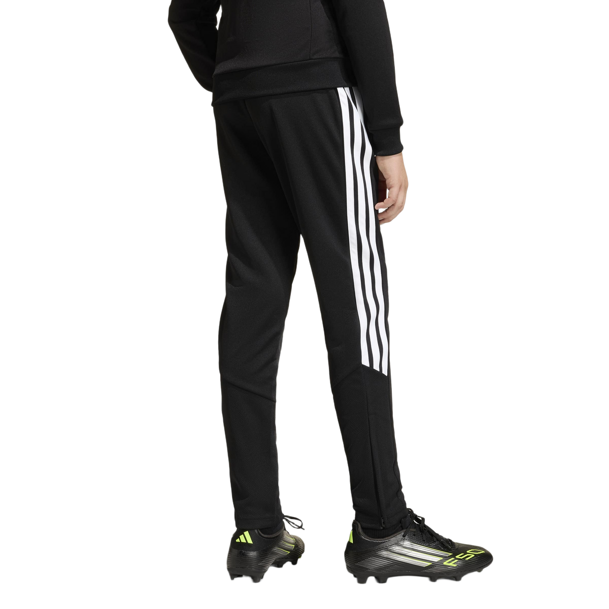 Rear view of a person in black Adidas track pants with white stripes and black F50 soccer cleats with neon accents on a white background.