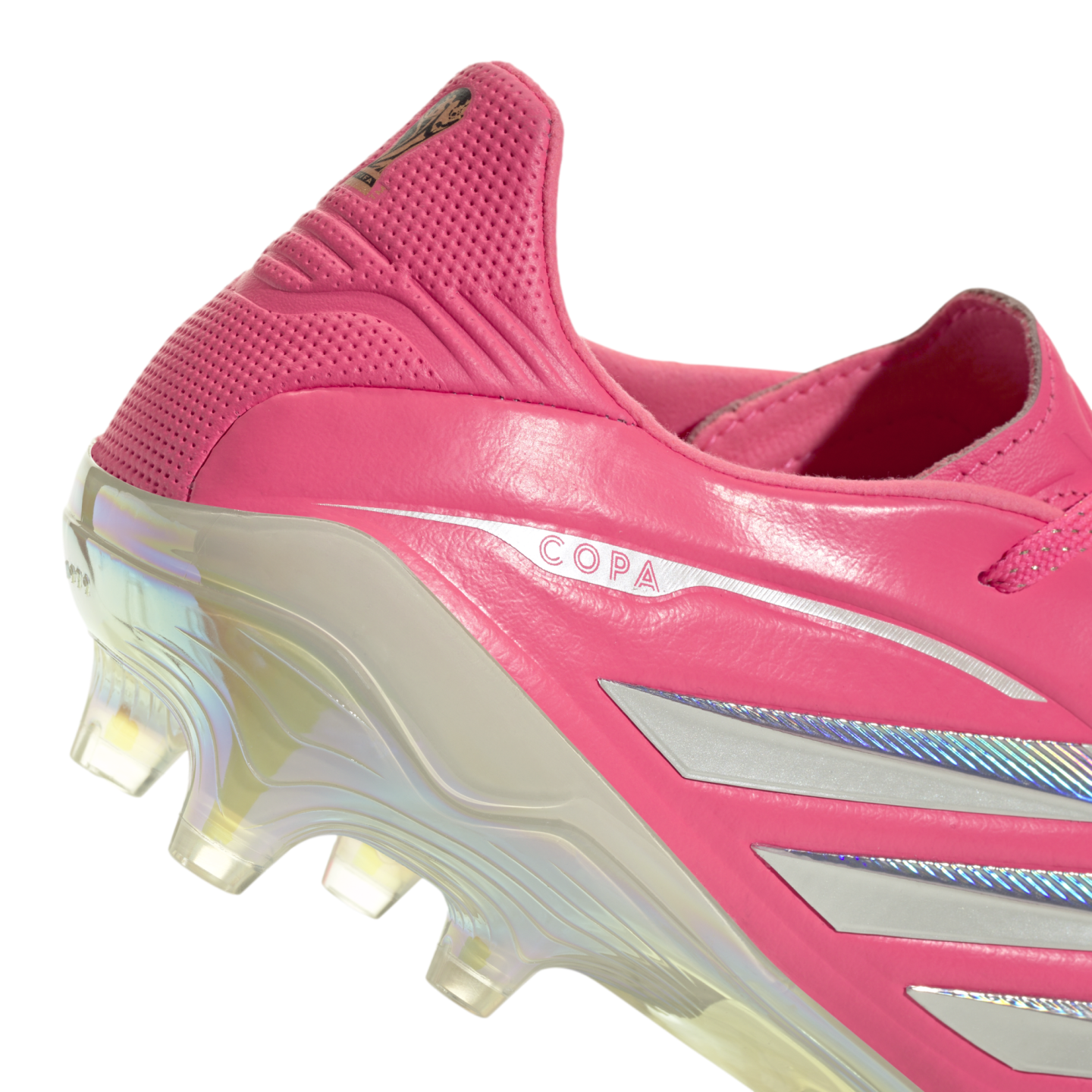 Close-up of the heel of a pink soccer cleat featuring silver "COPA" branding, silver stripes, and an iridescent translucent soleplate with studs.