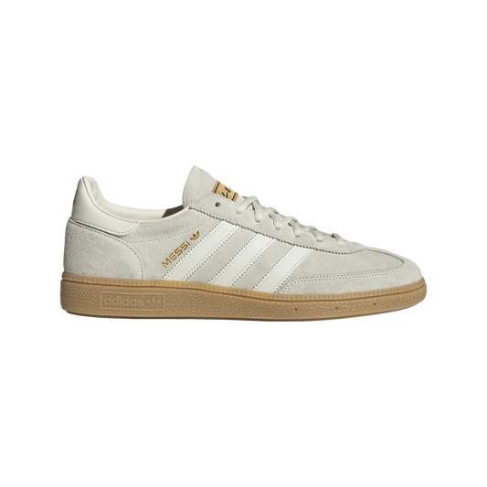 A light grey suede Adidas sneaker featuring white stripes, a gum sole, and "MESSI" in gold lettering on the side.