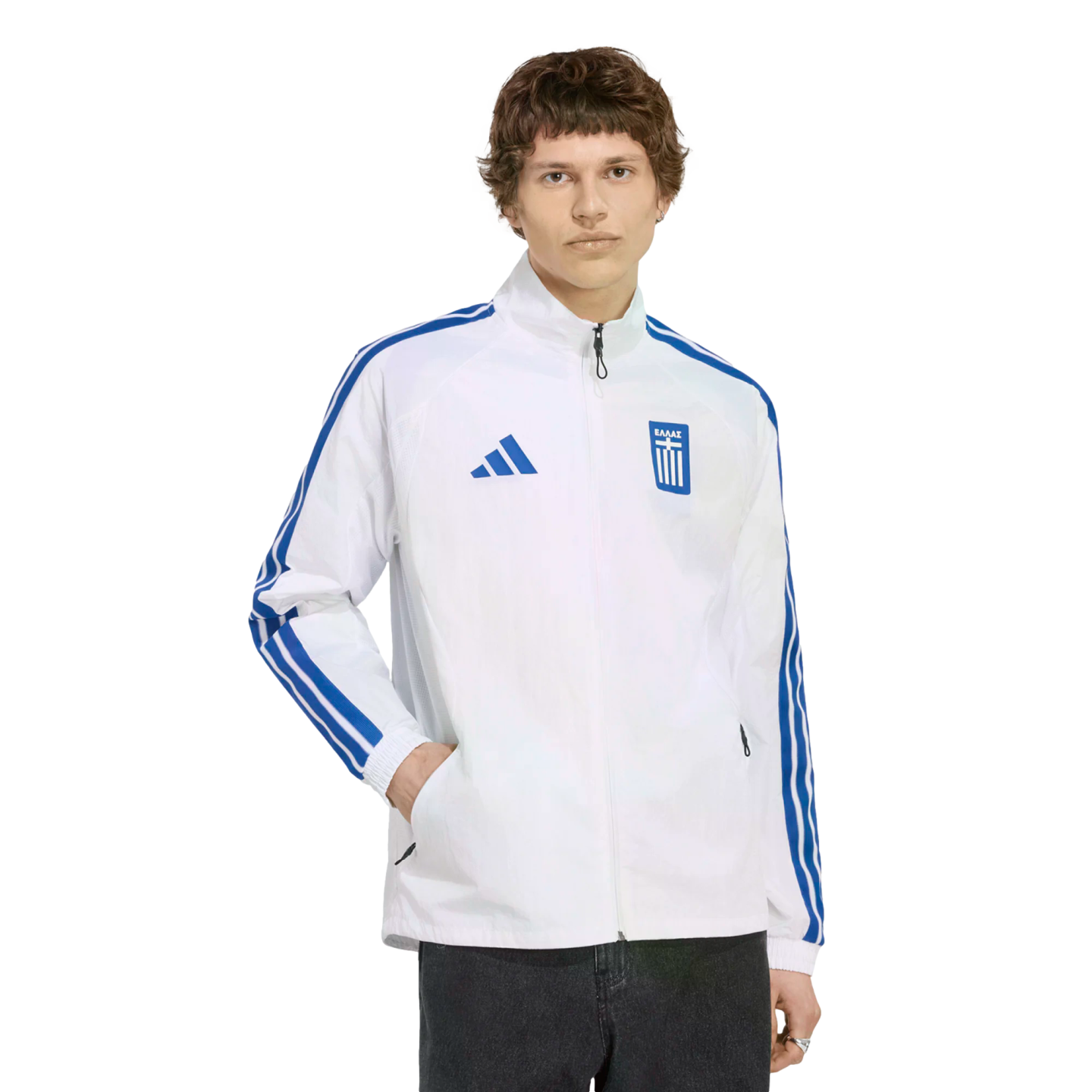 A young man wearing a white Adidas track jacket with blue stripes and a Greek national team crest, standing against a solid black background.