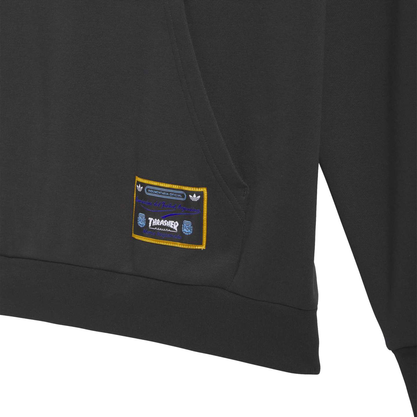 Close-up of a dark gray hoodie with a woven rectangular patch. The patch has a gold border and includes the Thrasher logo and Argentine Football Association text.