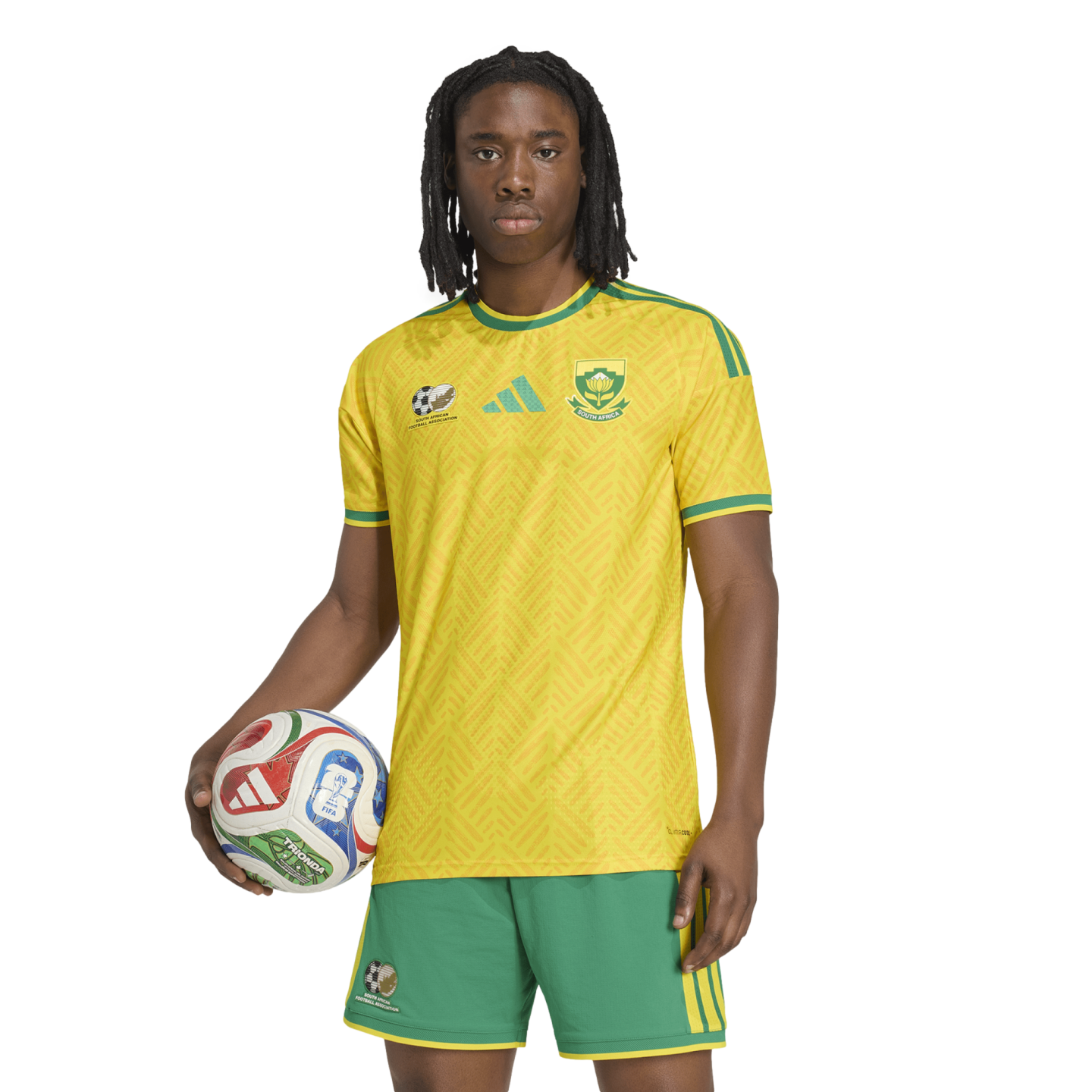 A person with dreadlocks wearing a yellow South African soccer kit, holding a soccer ball against a white background.