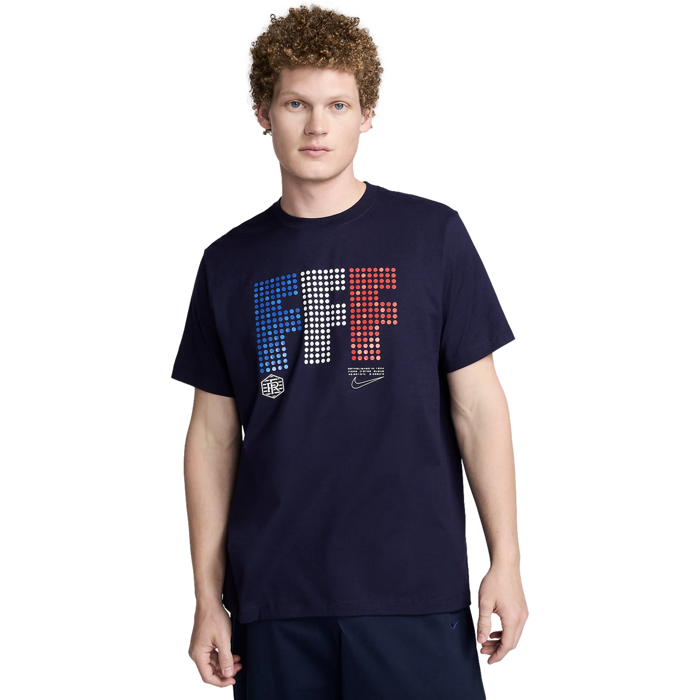 A man with curly hair wearing a navy blue Nike France t-shirt with a dotted "FFF" graphic in blue, white, and red.