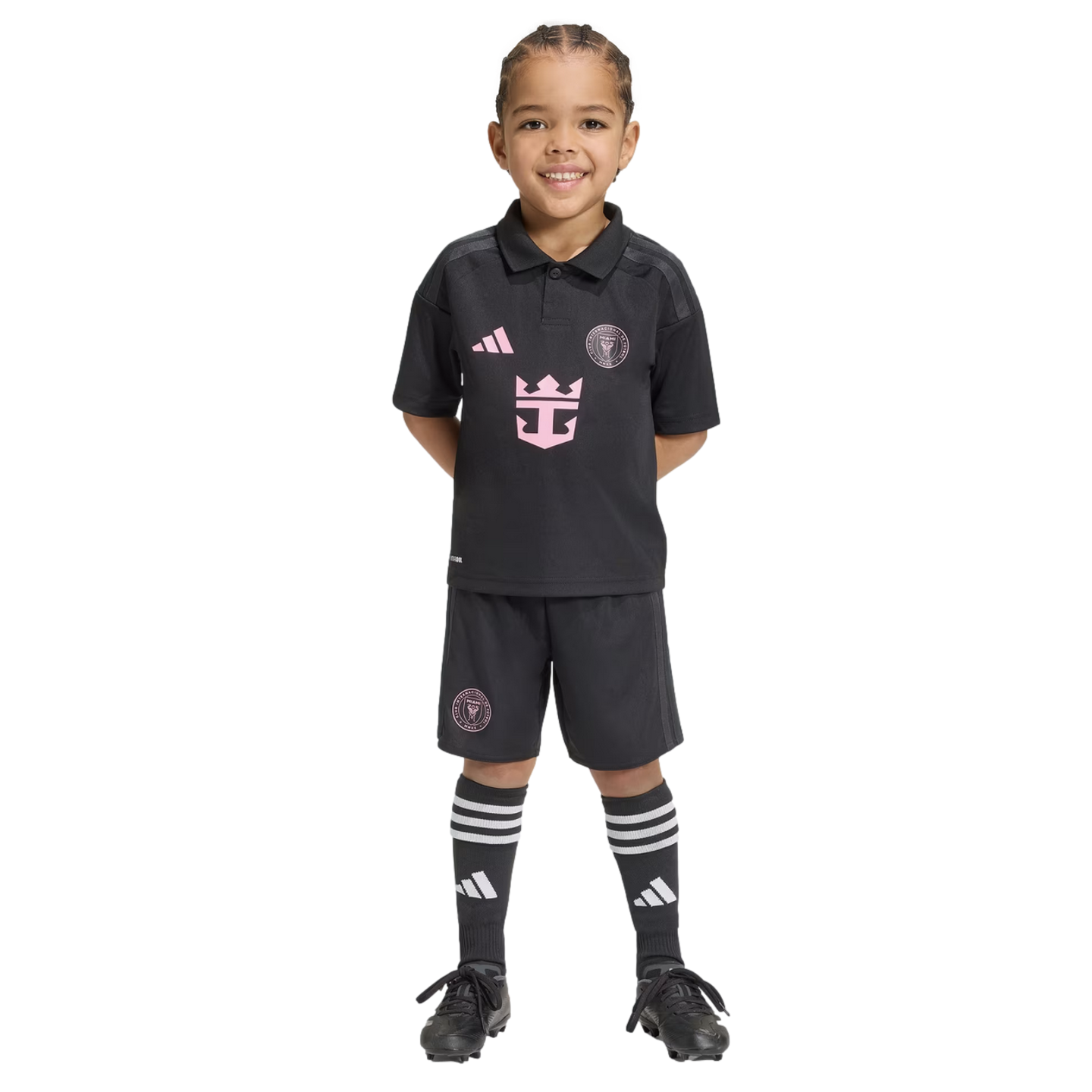 A young child smiling in a black Inter Miami CF soccer kit with pink logos, matching shorts, and tall socks, set against a black background.