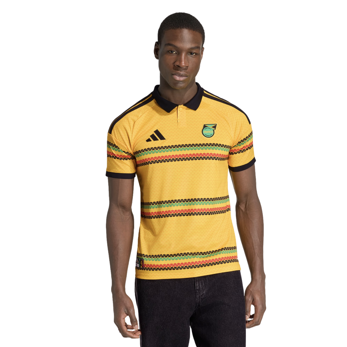 A man modeling a yellow Jamaica soccer jersey with a black polo collar and horizontal green, red, and black striped patterns against a black background.
