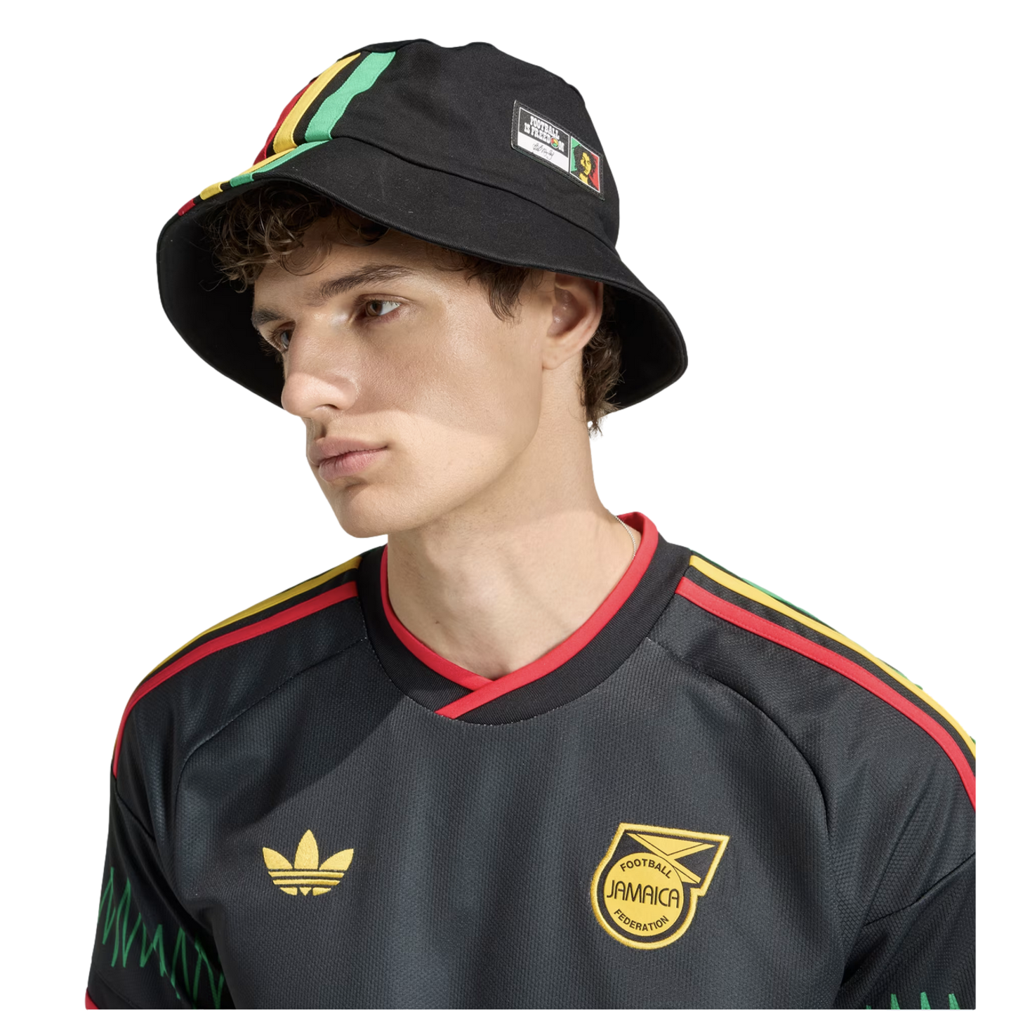 Young man in a black Adidas Jamaica soccer jersey and matching bucket hat with green, yellow, and red accents, posed against a solid black background.