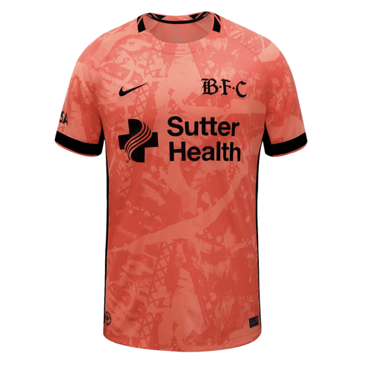 Peach soccer jersey with an abstract pattern and black Nike, 'B.F.C' gothic, and Sutter Health logos. Black trim on collar and sleeves.