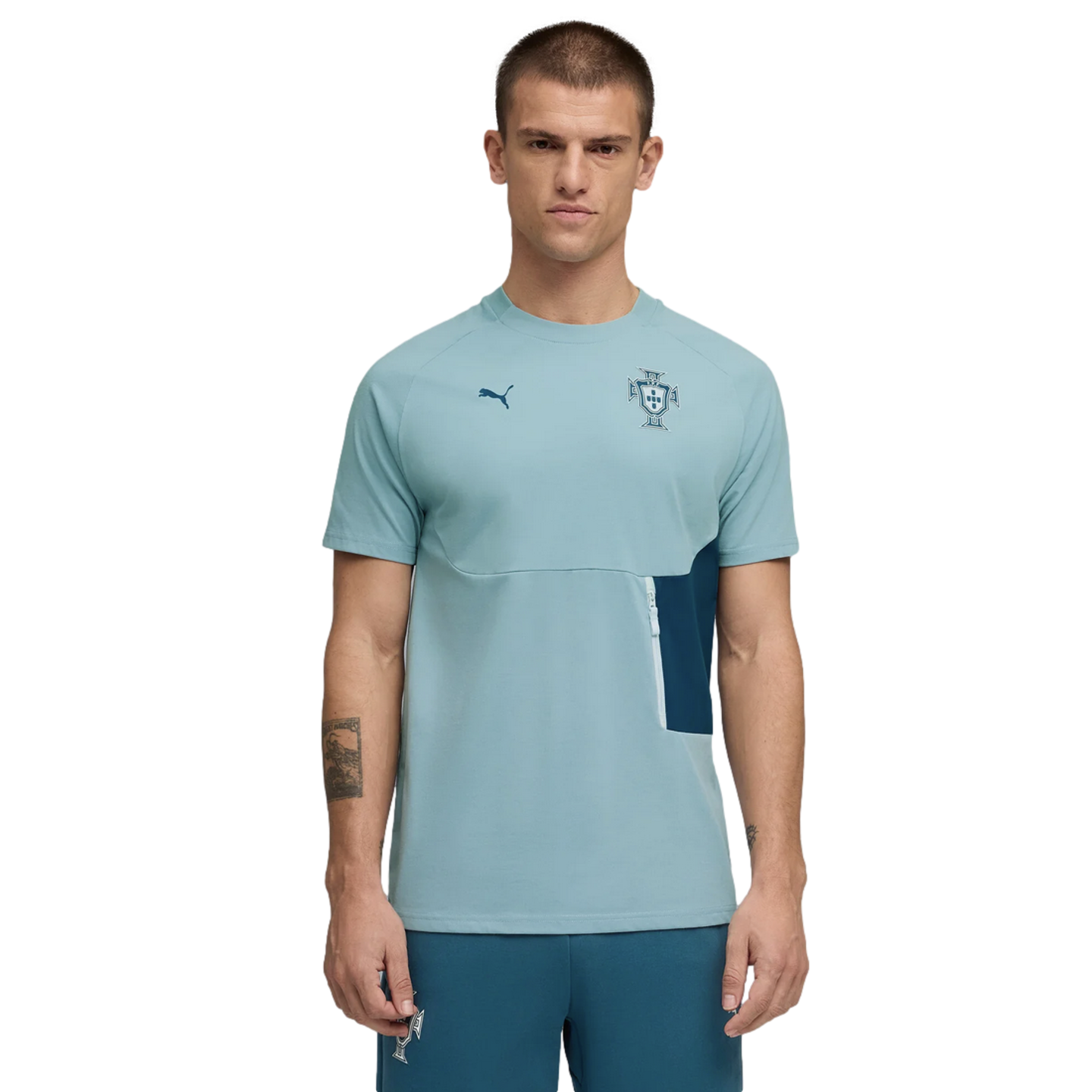 A studio photograph of a man modeling a light teal short-sleeved Puma training t-shirt with a Portuguese Football Federation crest on the chest, paired with matching teal pants, against a solid black background.