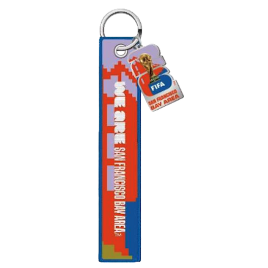 A keychain featuring a long blue fabric strap and a smaller charm. The strap has a red and purple pixelated design and white text that reads "WE ARE SAN FRANCISCO BAY AREA". The smaller charm displays the FIFA World Cup 26 logo, a gold trophy image, and "