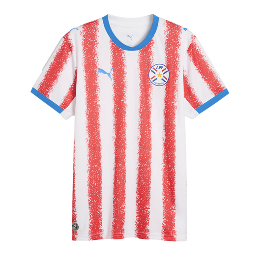 White football jersey with red spray-painted vertical stripes, blue collar and sleeve cuffs, blue Puma logo, and the APF Paraguay national team crest.