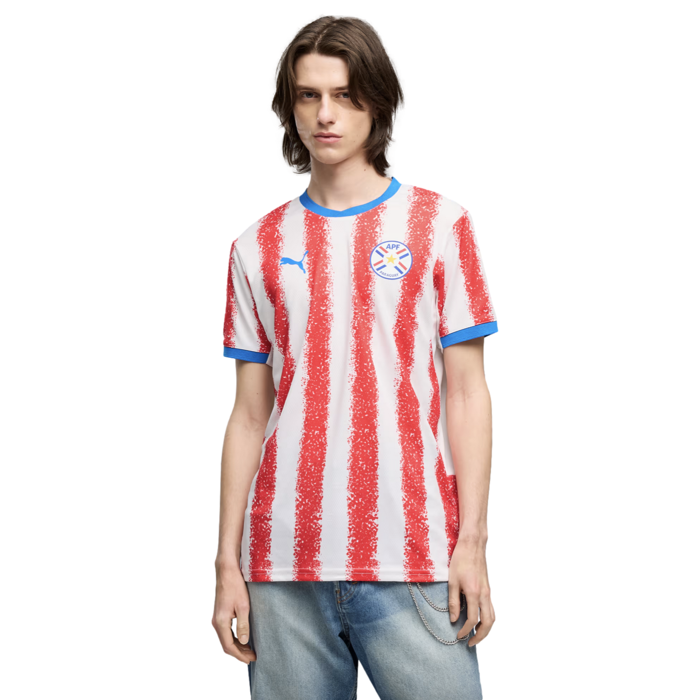 A man wearing a white and red vertically striped Paraguay national team soccer jersey and blue jeans, standing against a black background.