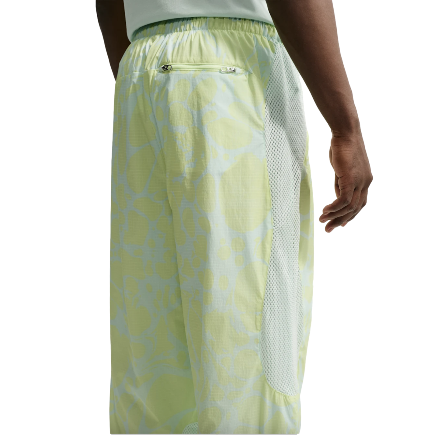 Rear view of a person wearing light green patterned athletic pants featuring white mesh side panels, an elastic waistband, and a small zippered back pocket.