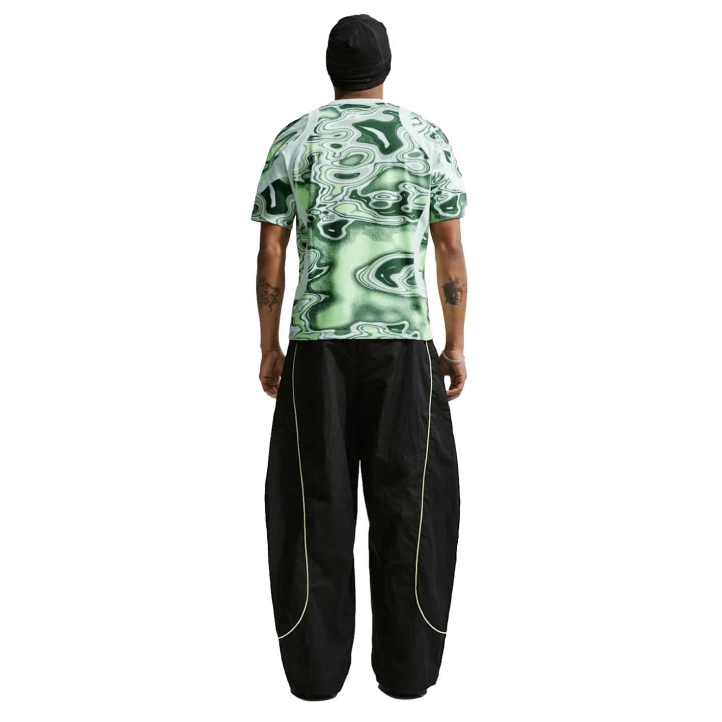 Back view of a person in a green patterned tee and baggy black pants with neon piping, against a white background.