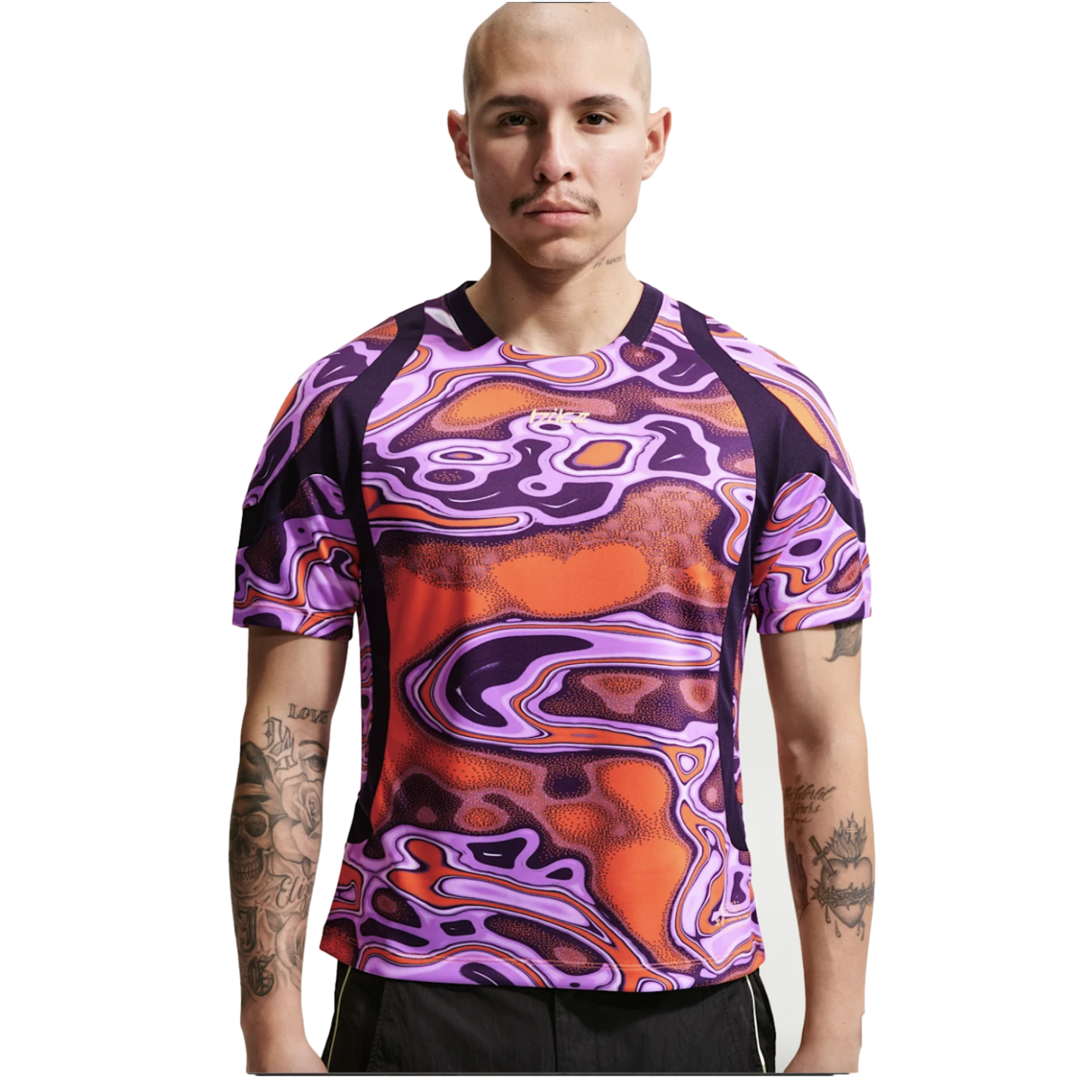 A bald man with arm tattoos wearing a vibrant purple and orange swirl-patterned athletic shirt.